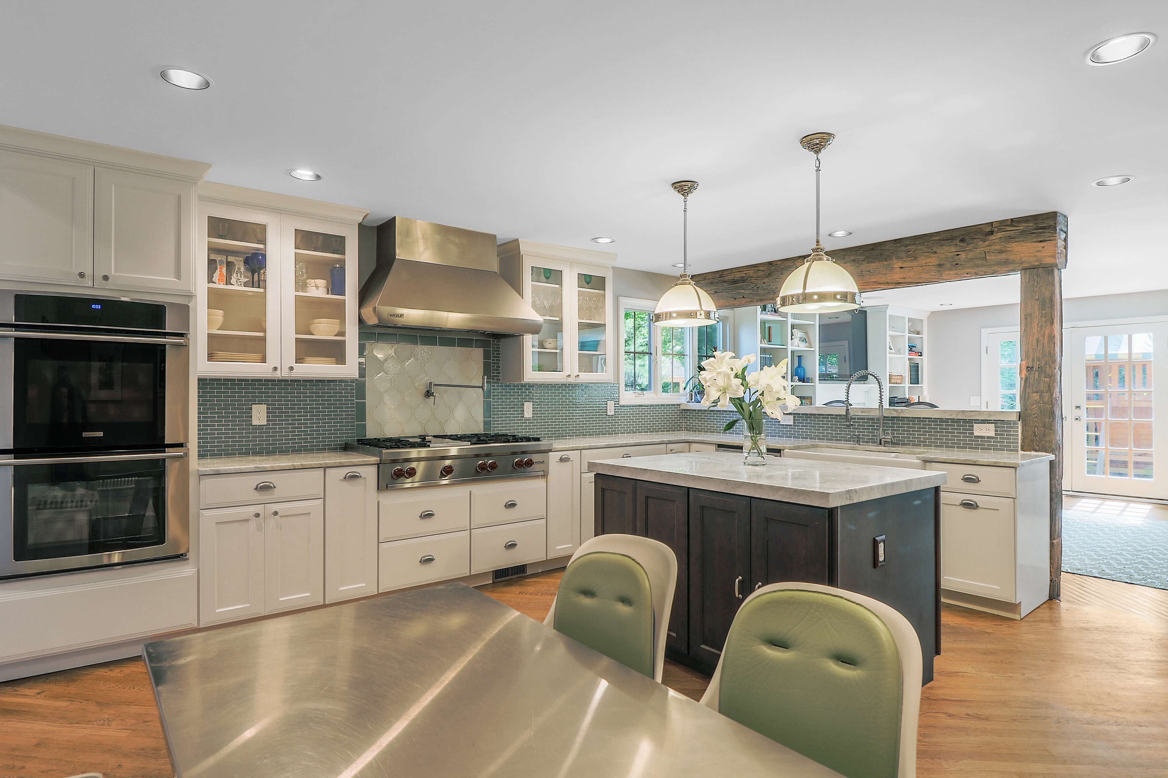 The image shows a modern kitchen with white cabinets, a gray tile backsplash, and an island featuring dark wood cabinetry and a marble countertop.