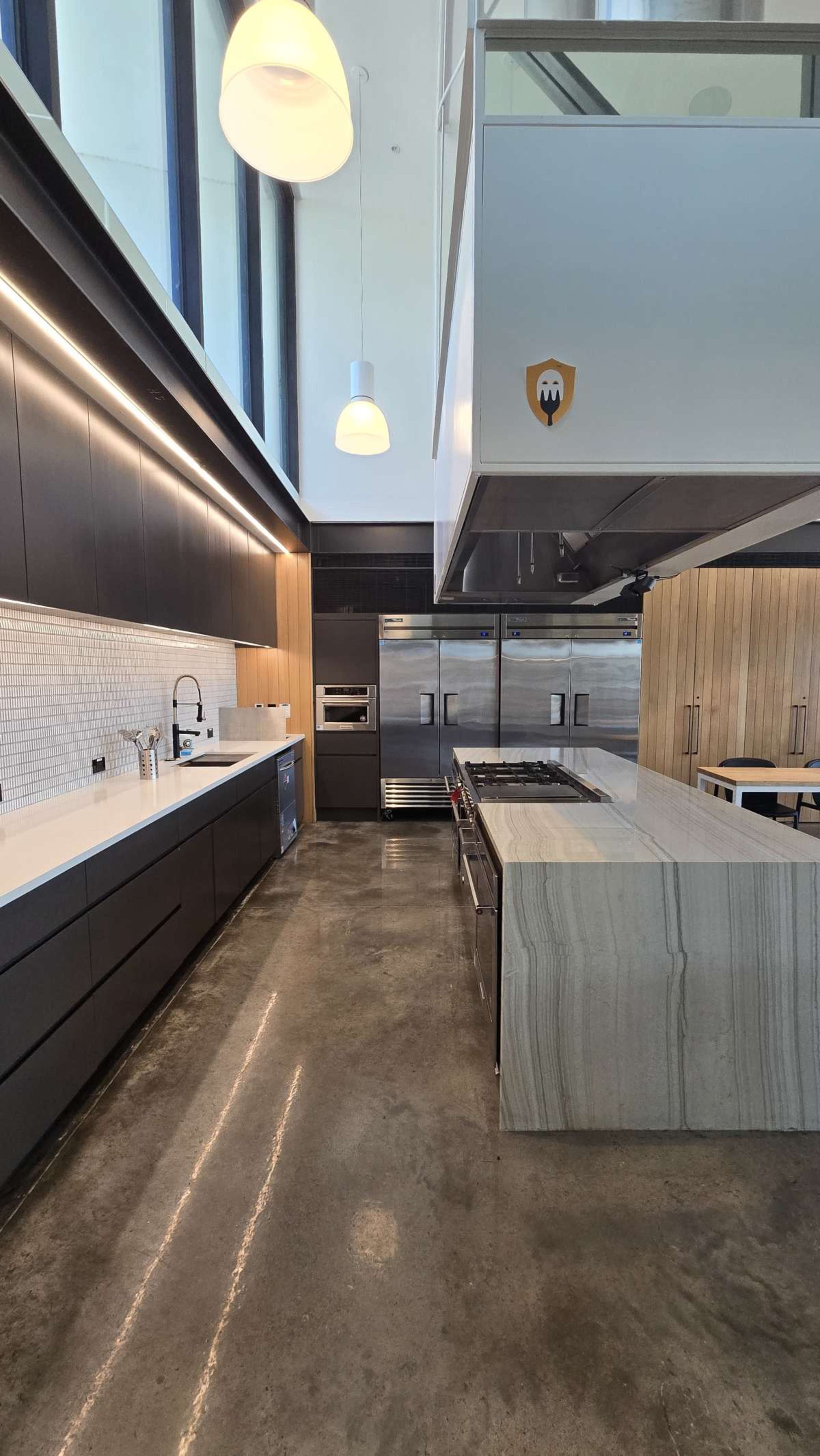 The image shows a modern kitchen with sleek black cabinetry, stainless steel appliances, and a large stone island.