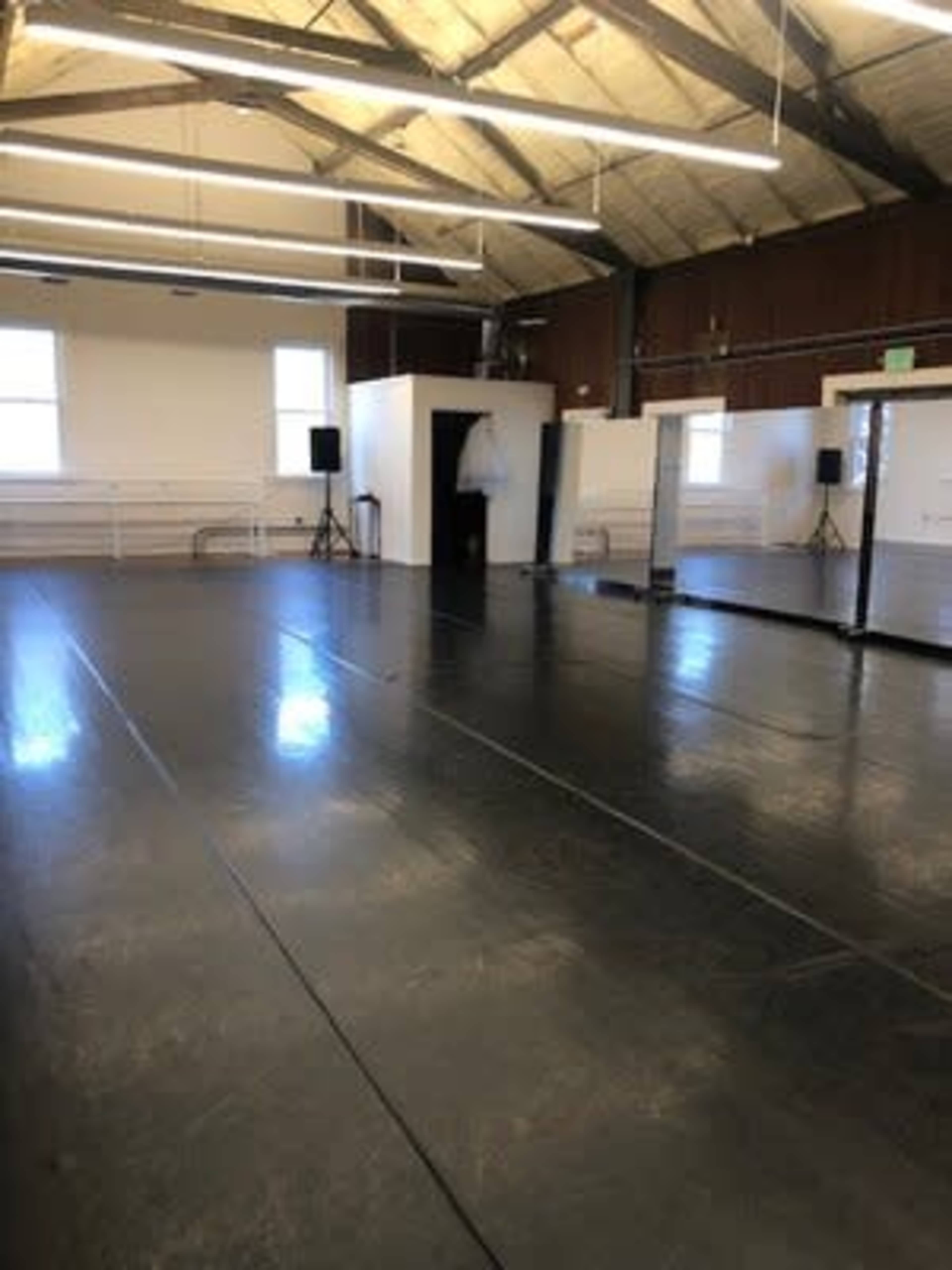 The image shows a spacious dance studio with a polished black floor, large mirrors on one wall, and wooden beams in the ceiling.