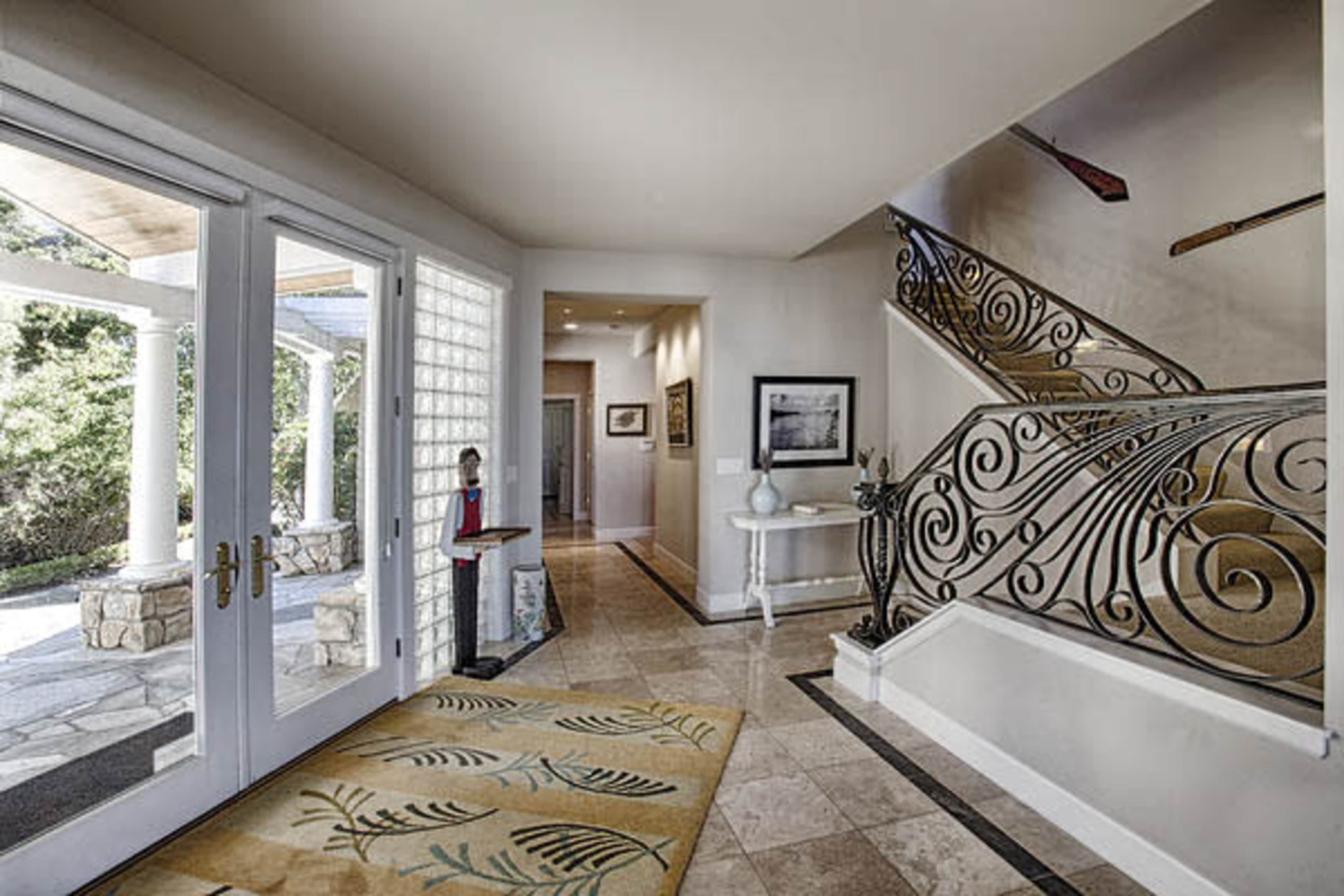 A well-lit entryway with a spiral staircase, decorative railing, and a view of a stone patio through glass doors.