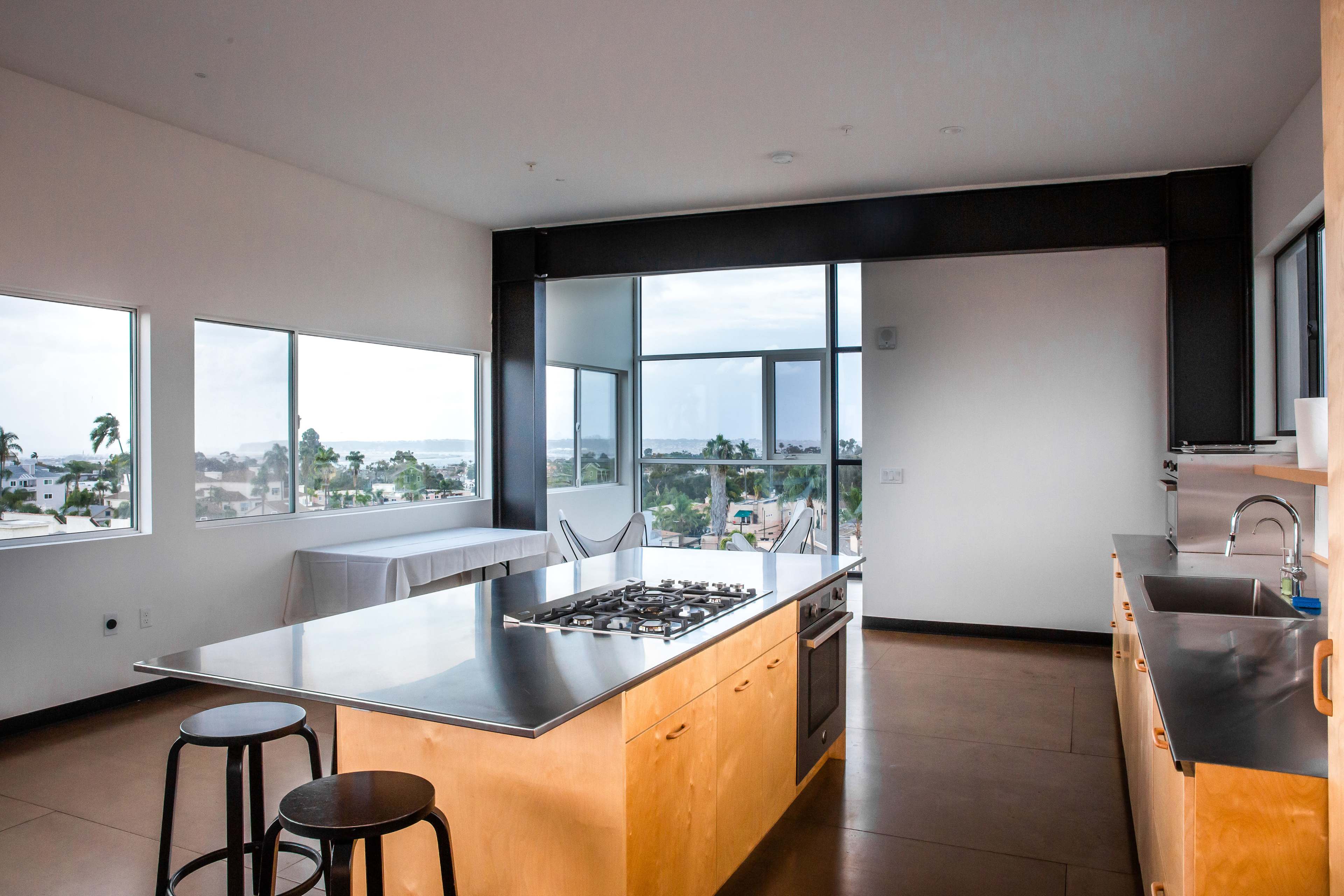 A modern kitchen features a center island with a gas cooktop, surrounded by large windows that offer a view of the outdoors.
