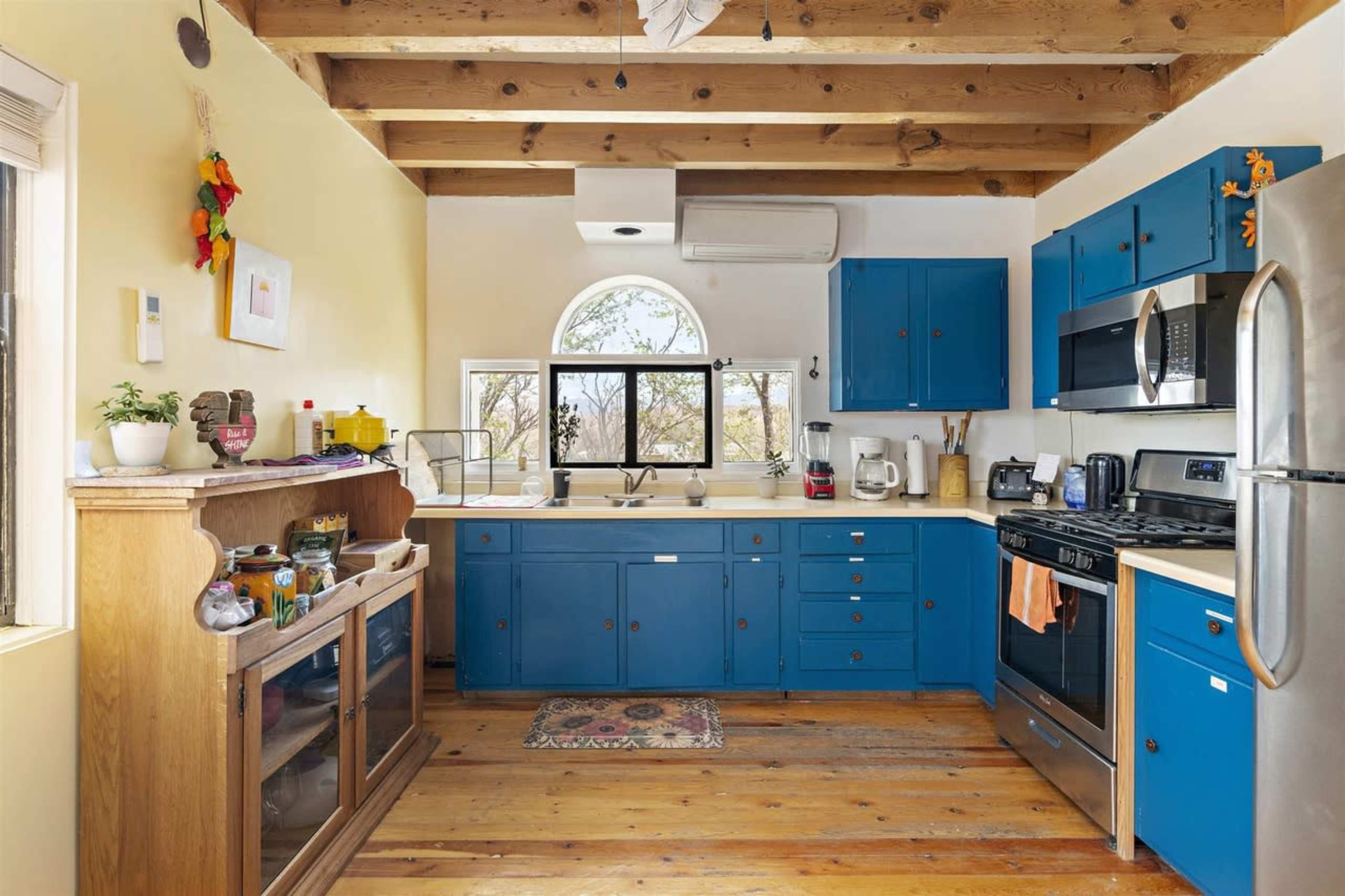 The kitchen features blue cabinetry, stainless steel appliances, and wooden beams on the ceiling.