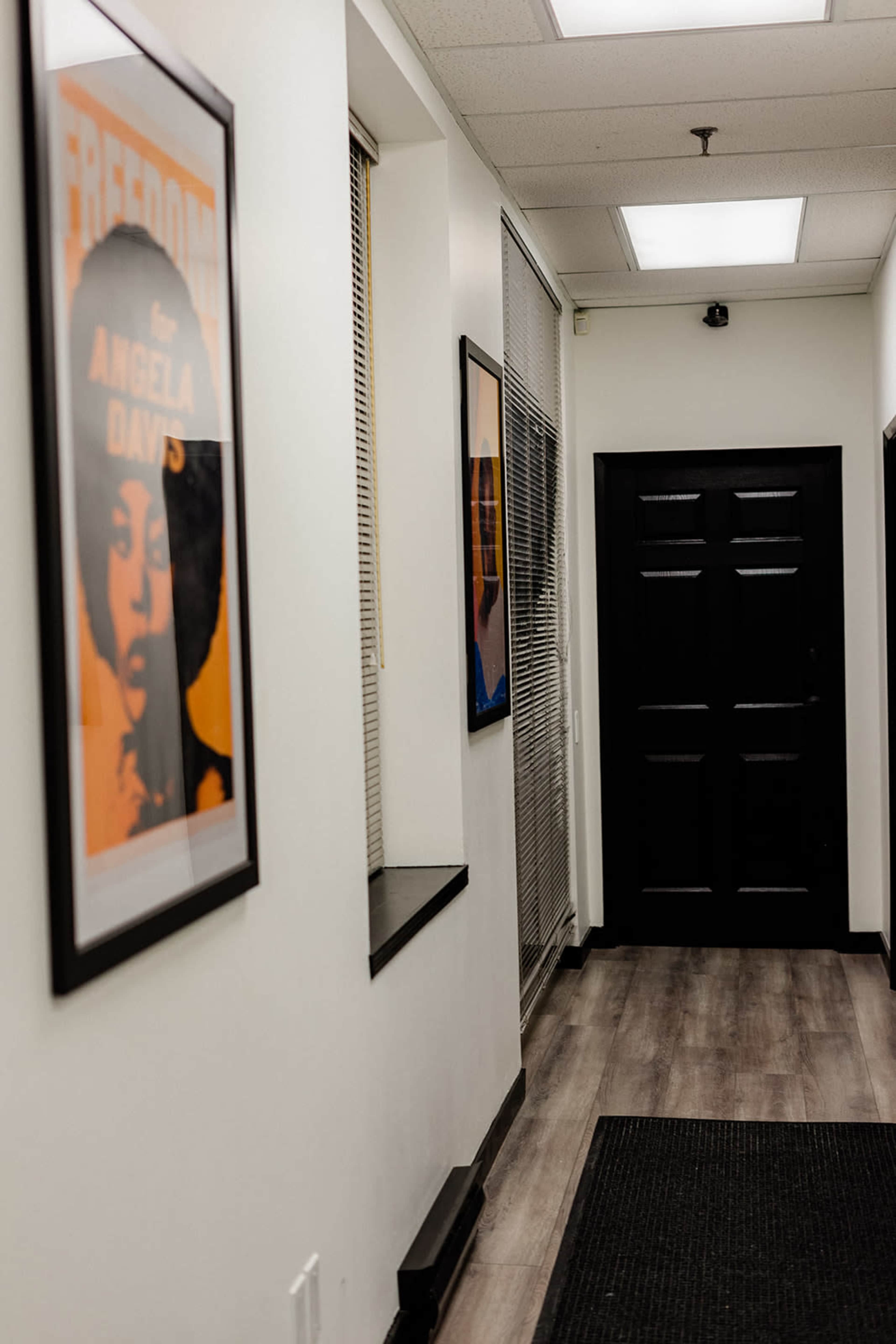 A hallway featuring framed posters on the walls, leading to a black door at the end.