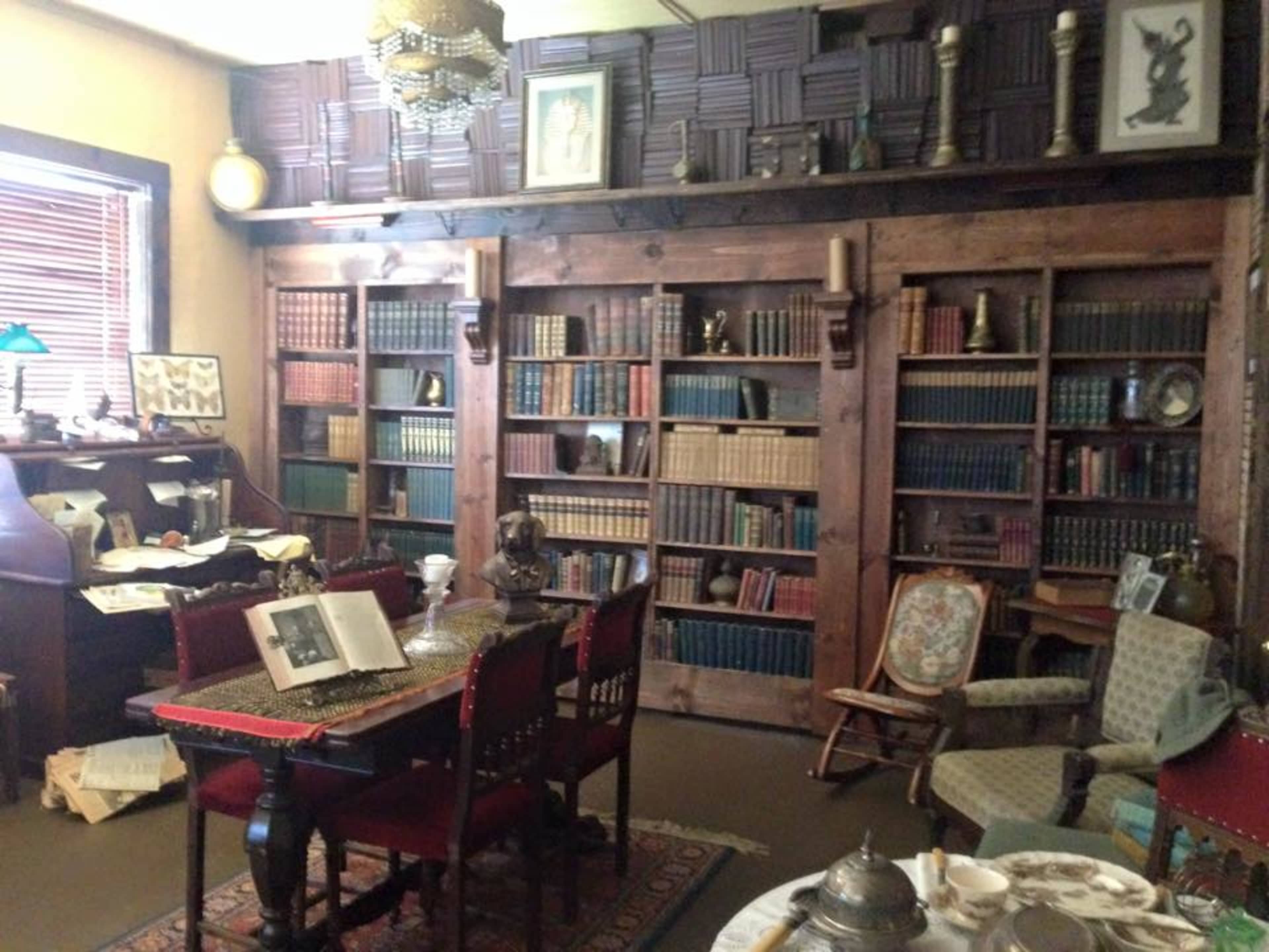 A vintage study with wooden bookshelves filled with books, a dining table with chairs, and various decorative items scattered throughout the room.