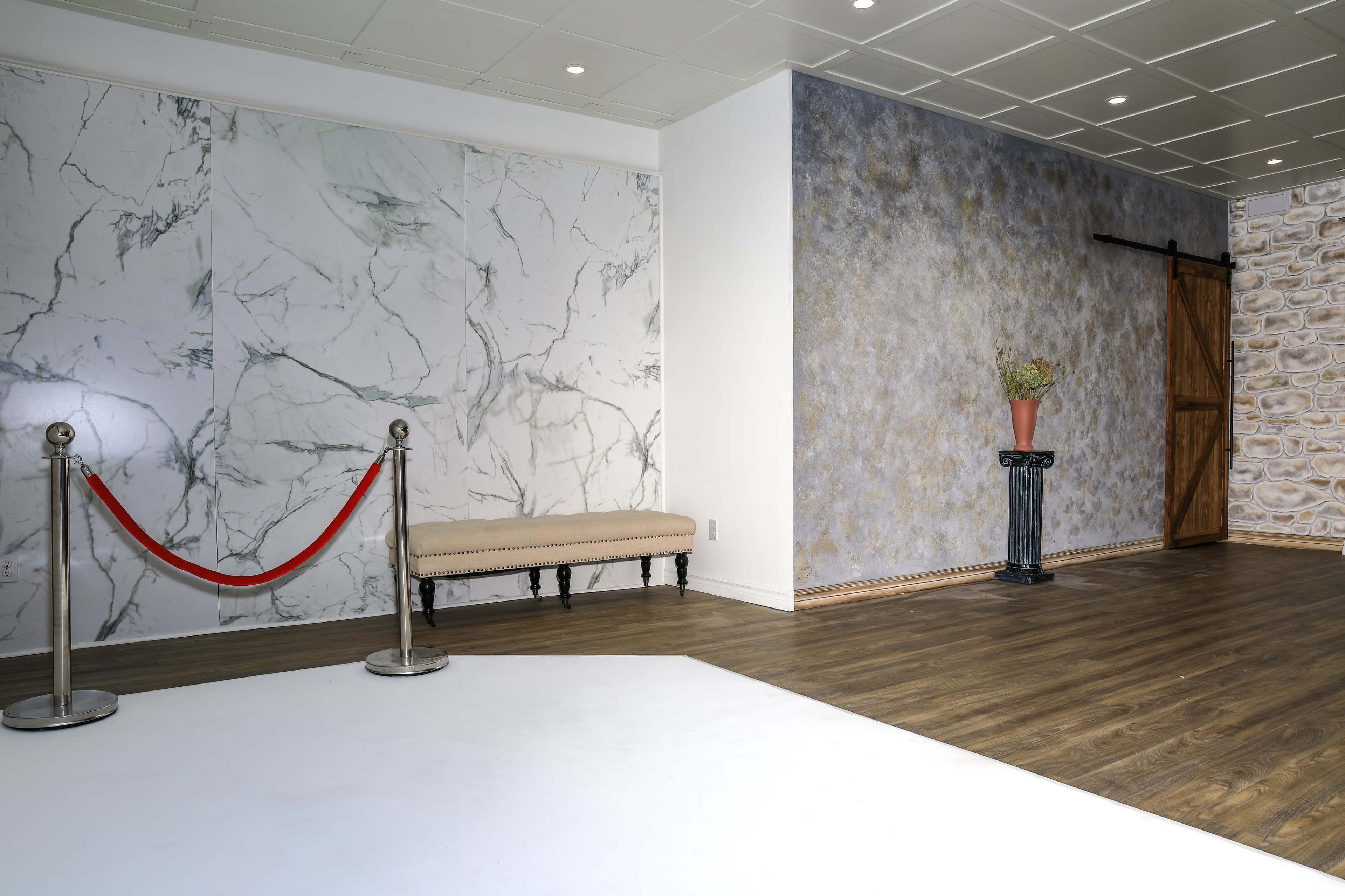A modern interior space featuring a bench with a marble backdrop, a stone-clad wall, and a decorative plant on a pedestal near a wooden sliding door.