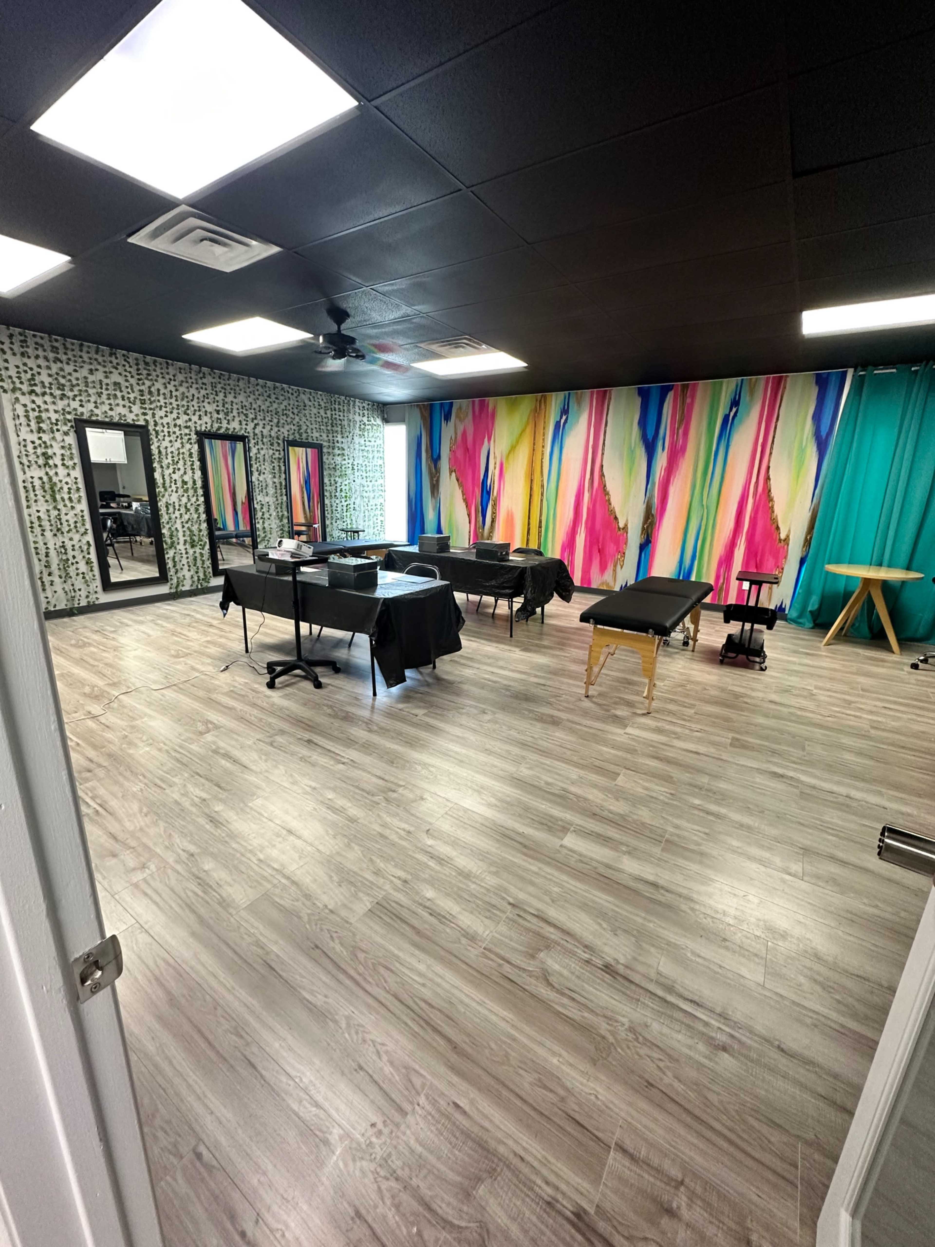 A spacious, brightly colored treatment room with wooden flooring, equipped with multiple tables covered in black cloth and vibrant wall art.