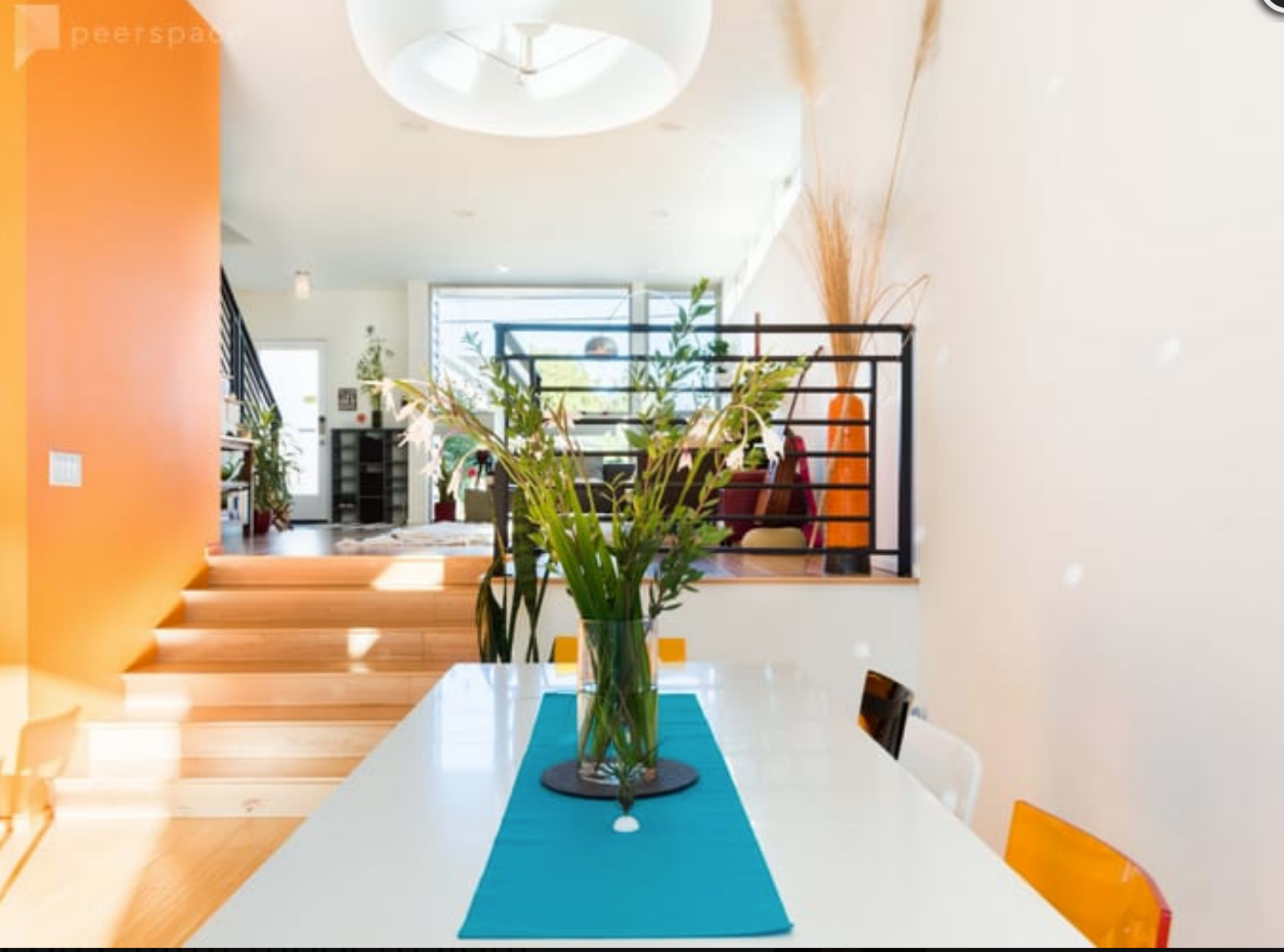 A modern dining area features a white table adorned with a teal runner and a centerpiece of plants, with an open space leading to a bright living room.