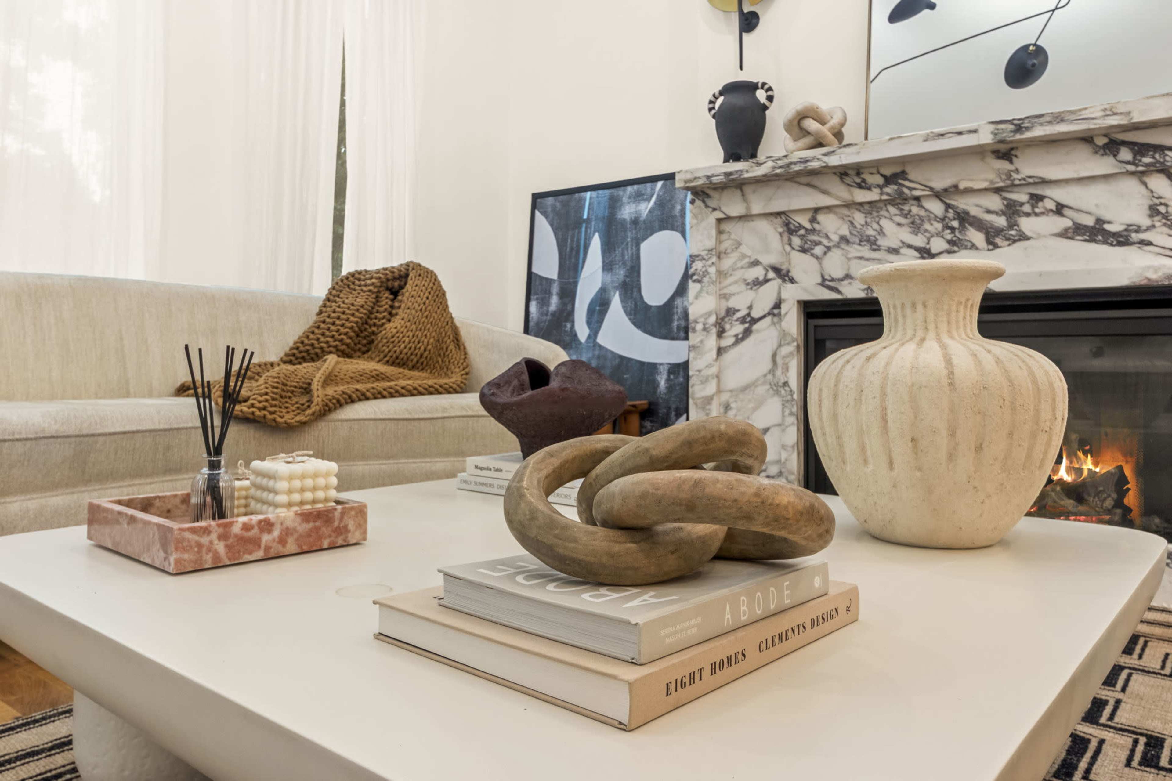 The image features a modern living room with a marble fireplace, a light sofa, and a coffee table adorned with books, decorative items, and a vase.