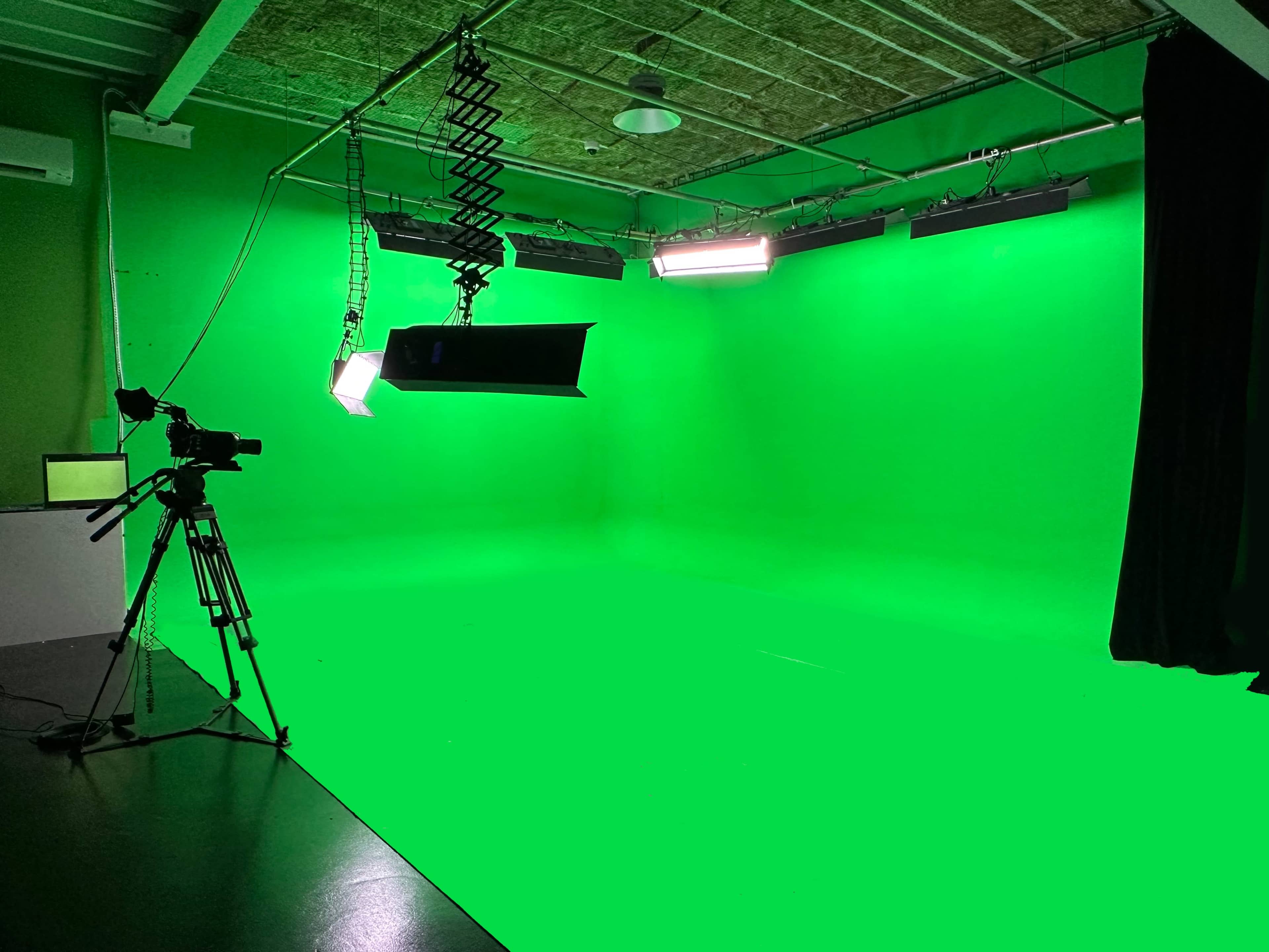 A green screen studio with a camera and lighting equipment set up.