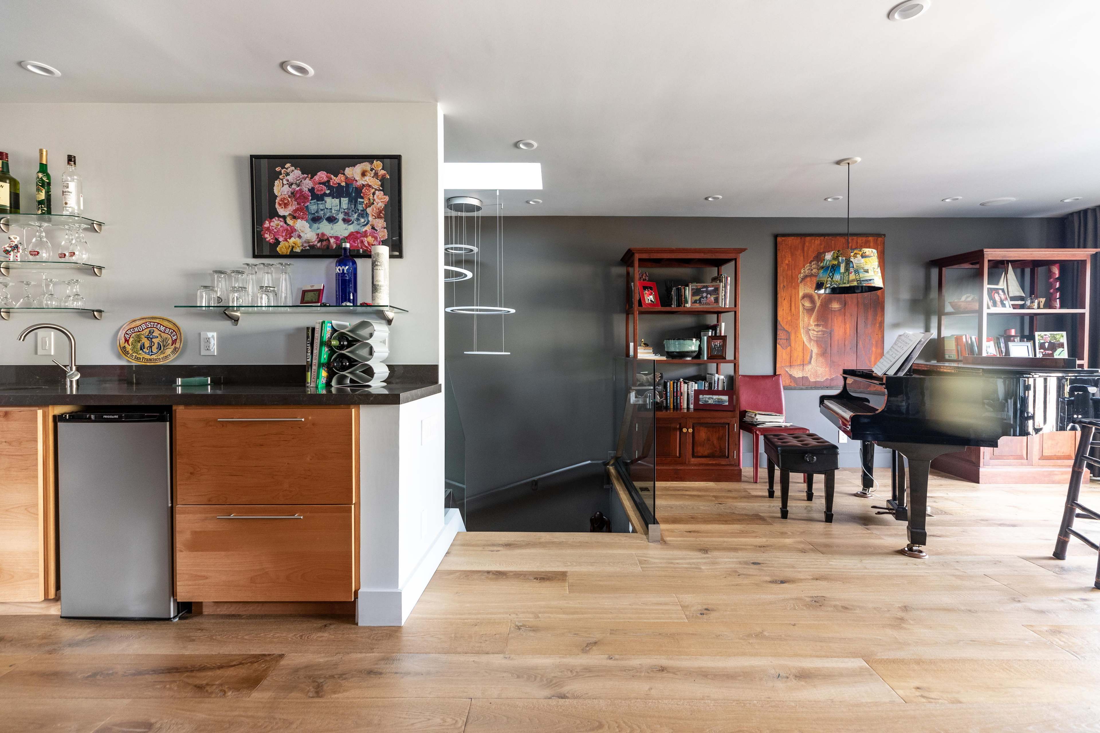 A modern interior featuring a kitchen area with a bar and a grand piano in a living space with wooden flooring and artistic decor.