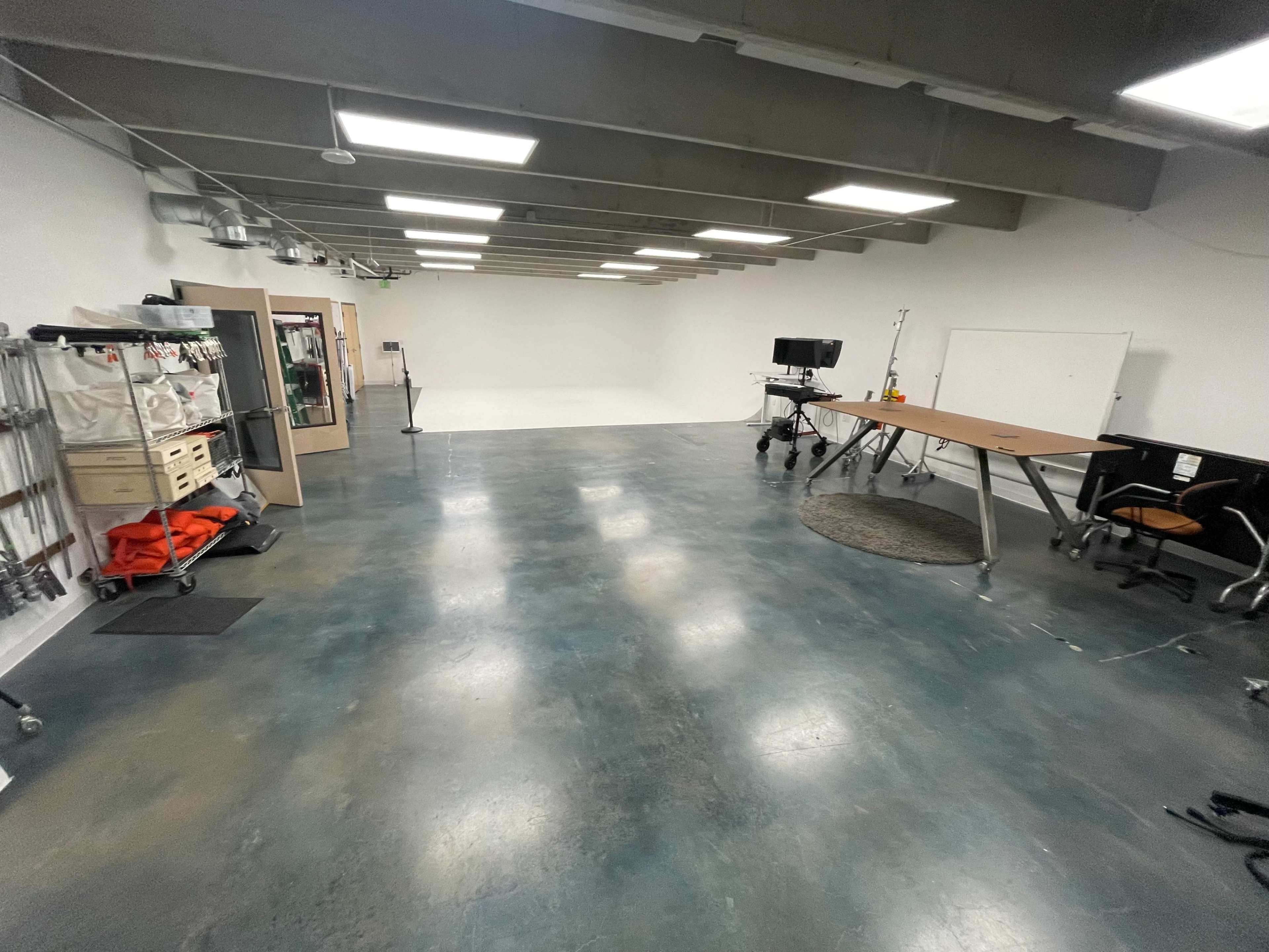 A spacious studio with a white backdrop, a desk with a chair, and various equipment along the walls.