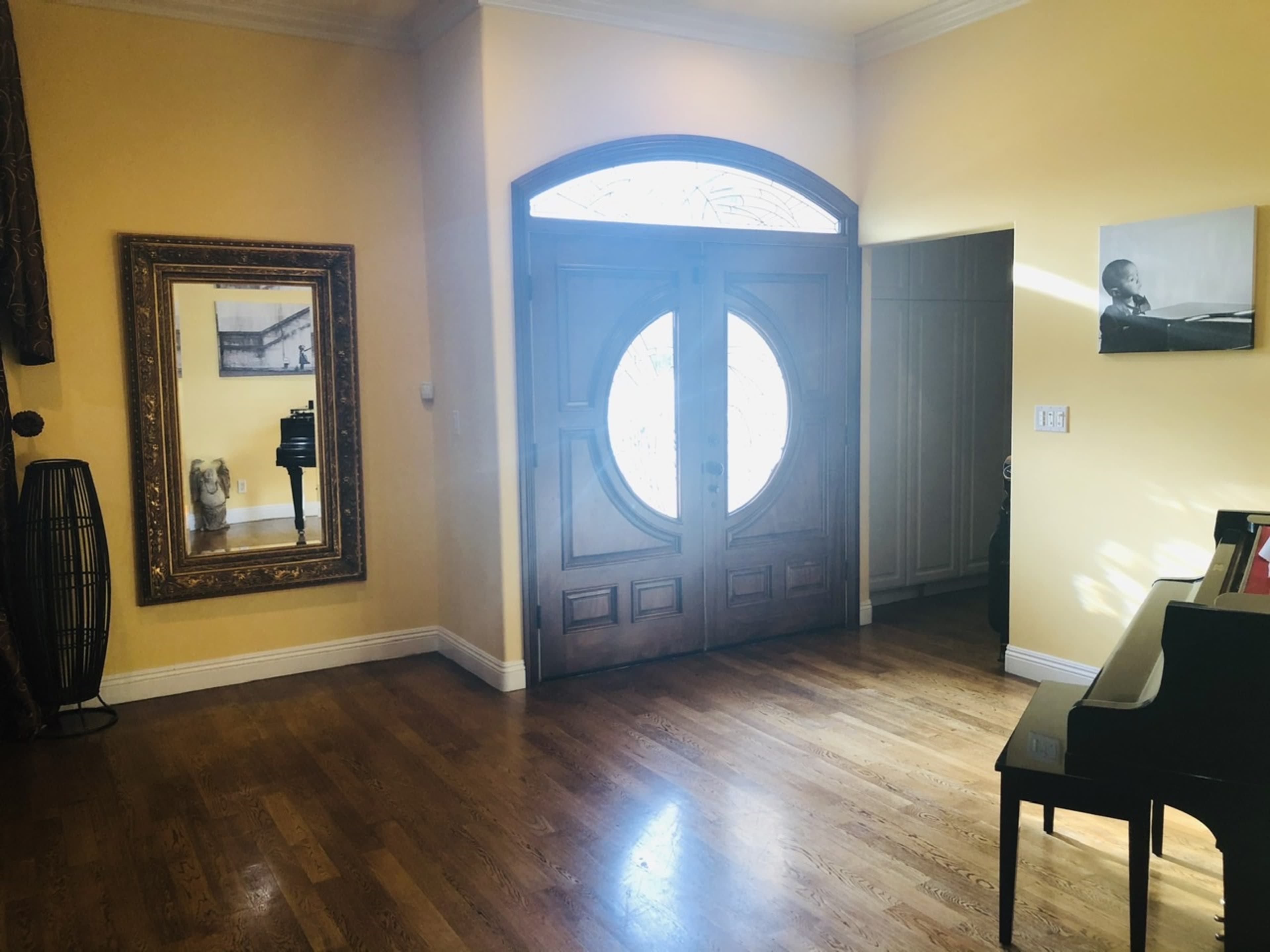 A bright foyer with a decorative mirror, wooden double doors, and a piano in a room with yellow walls.