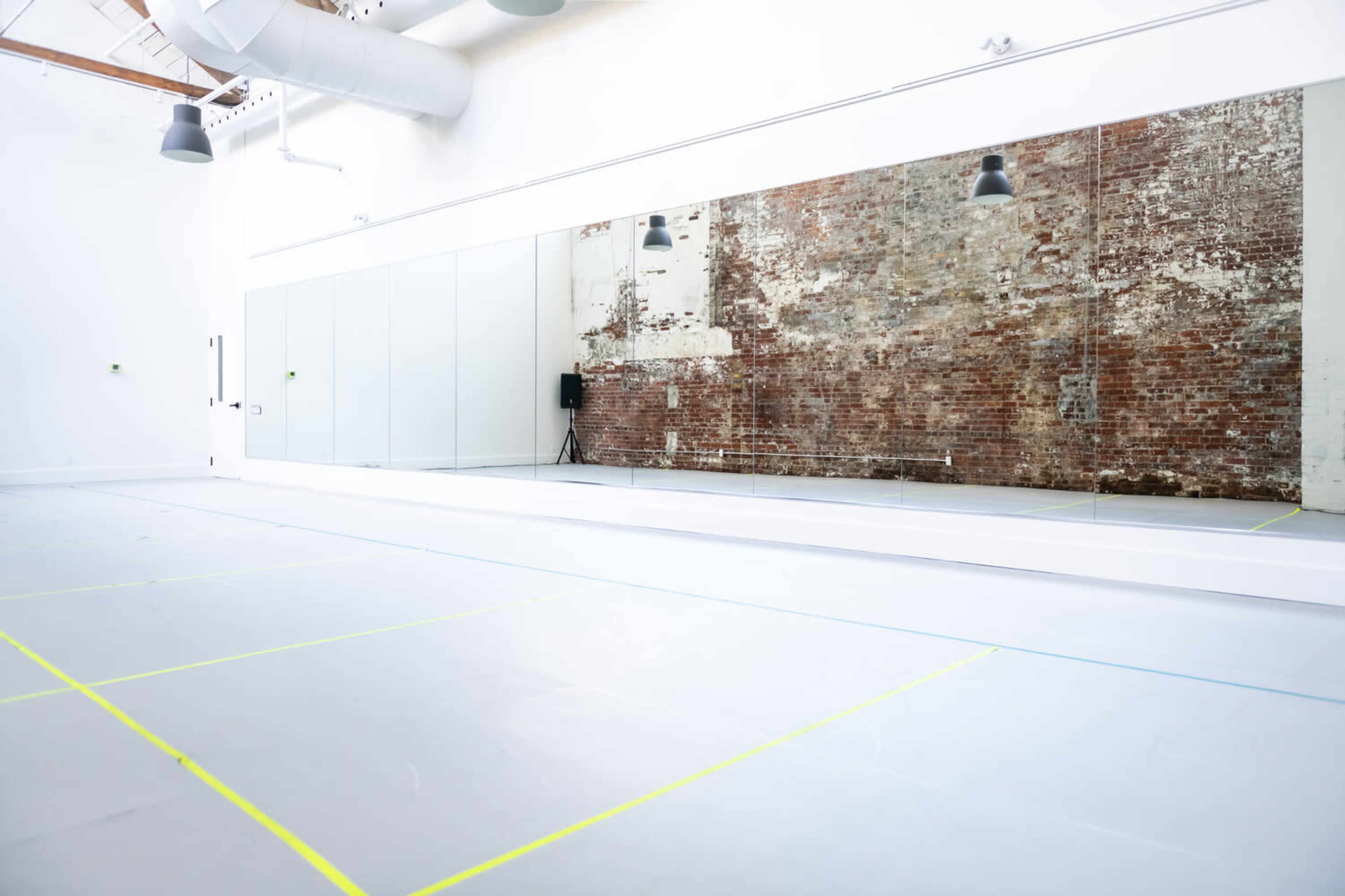 A spacious dance studio with large mirrors, exposed brick walls, and marked flooring.