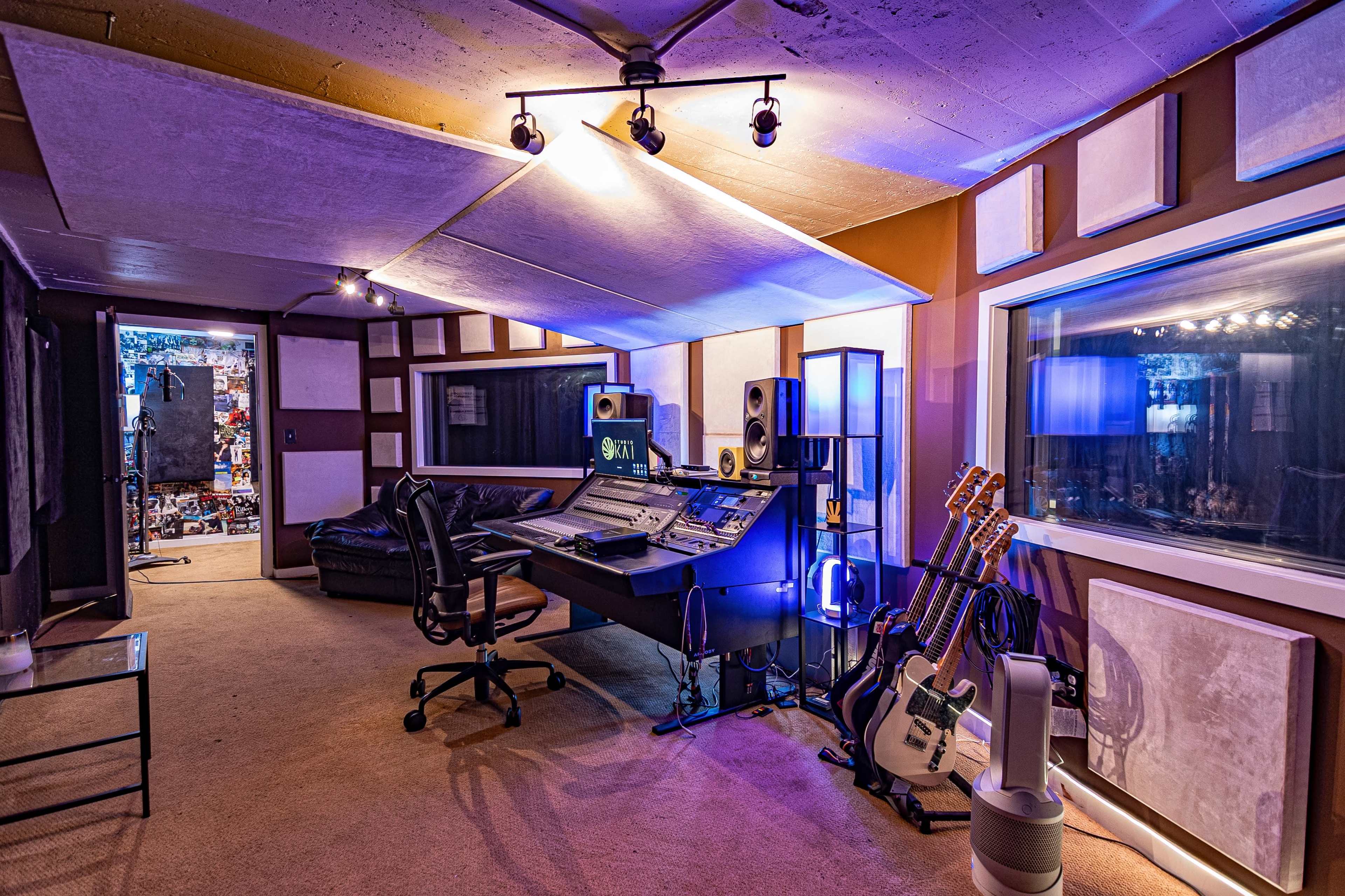 A recording studio features a central mixing desk, musical instruments, and soundproofing panels.
