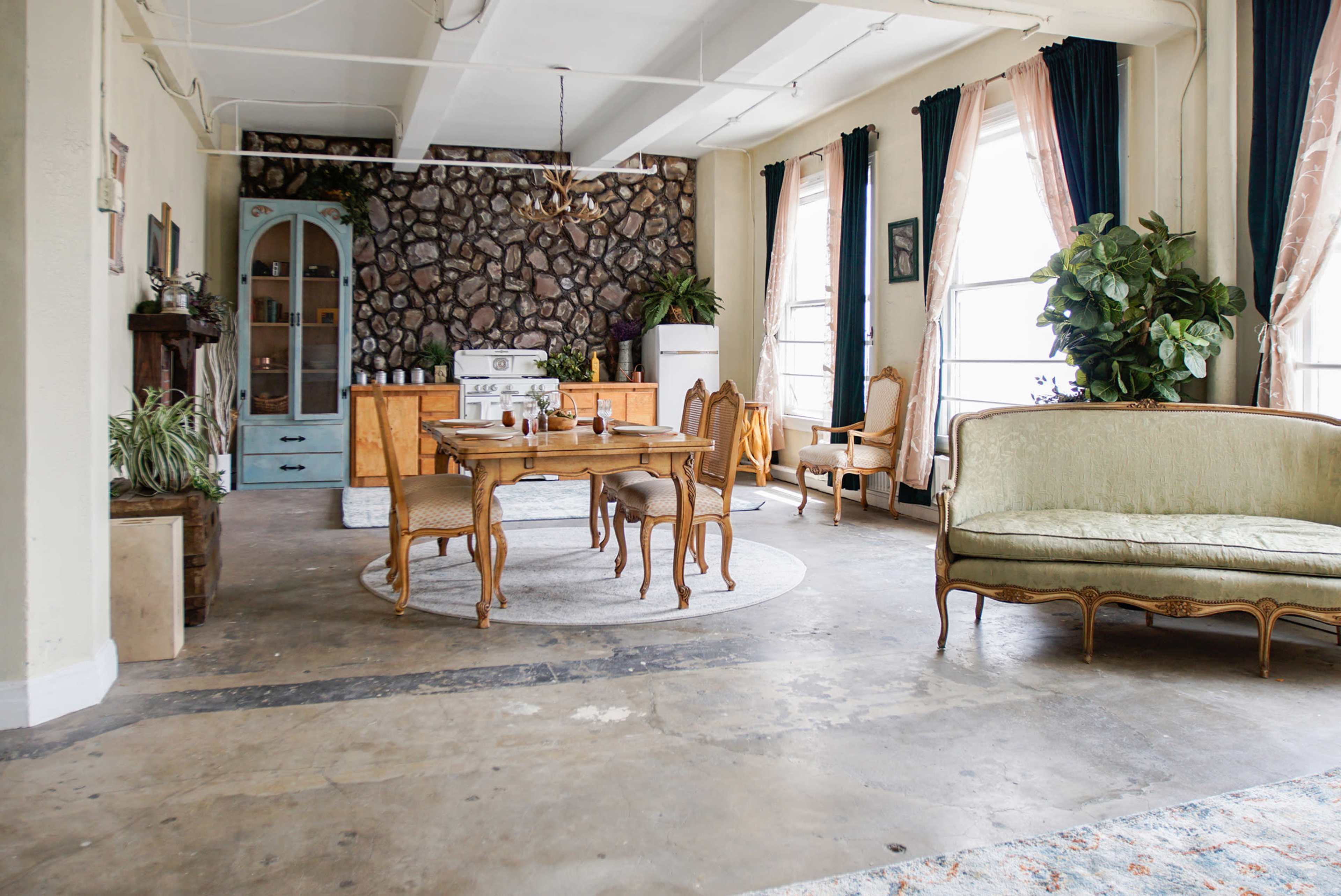 A spacious, light-filled interior featuring a dining table surrounded by chairs, a green sofa, and a stone accent wall.