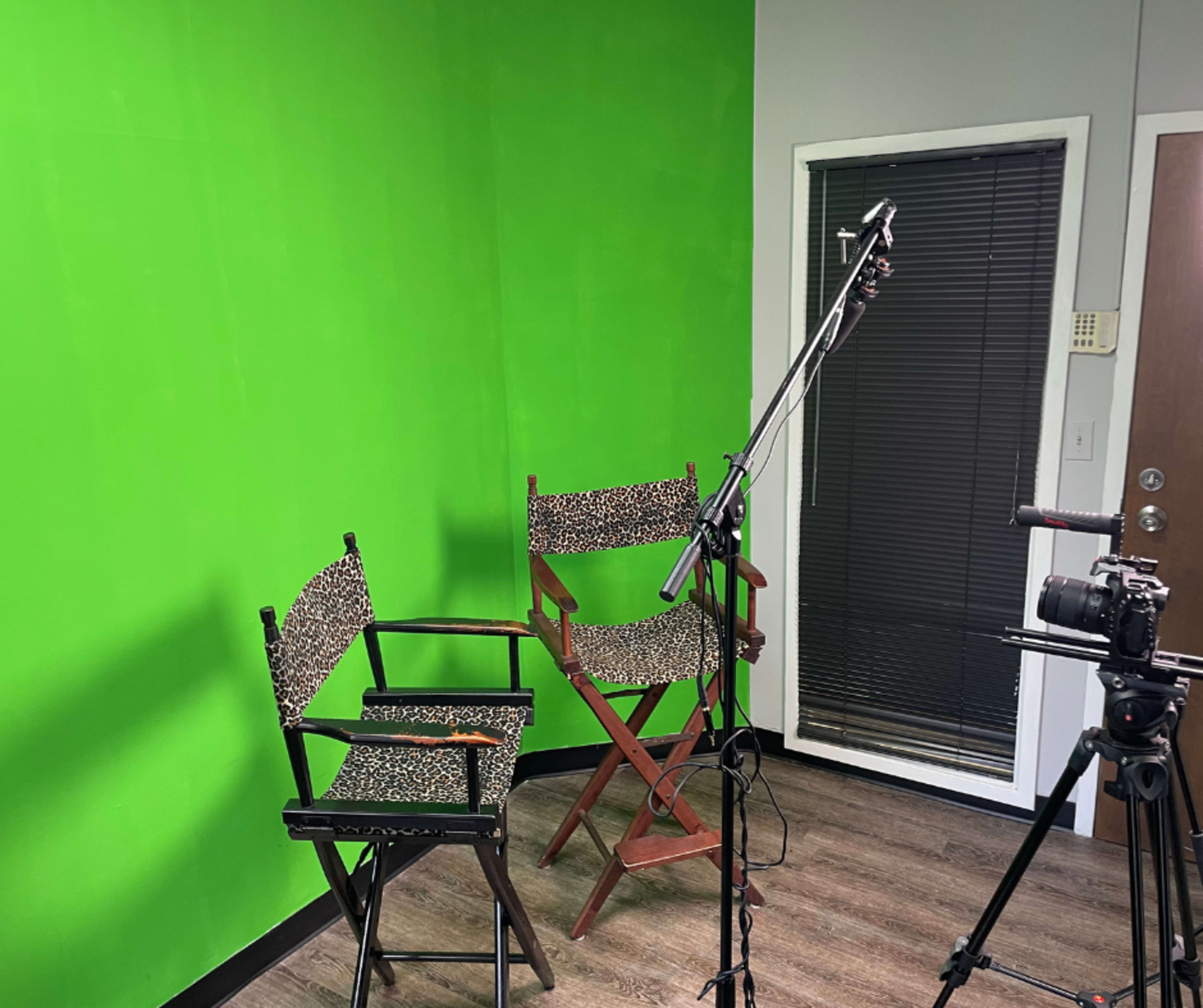 A room with a bright green wall, two chairs with patterned fabric, and a camera positioned on a tripod.