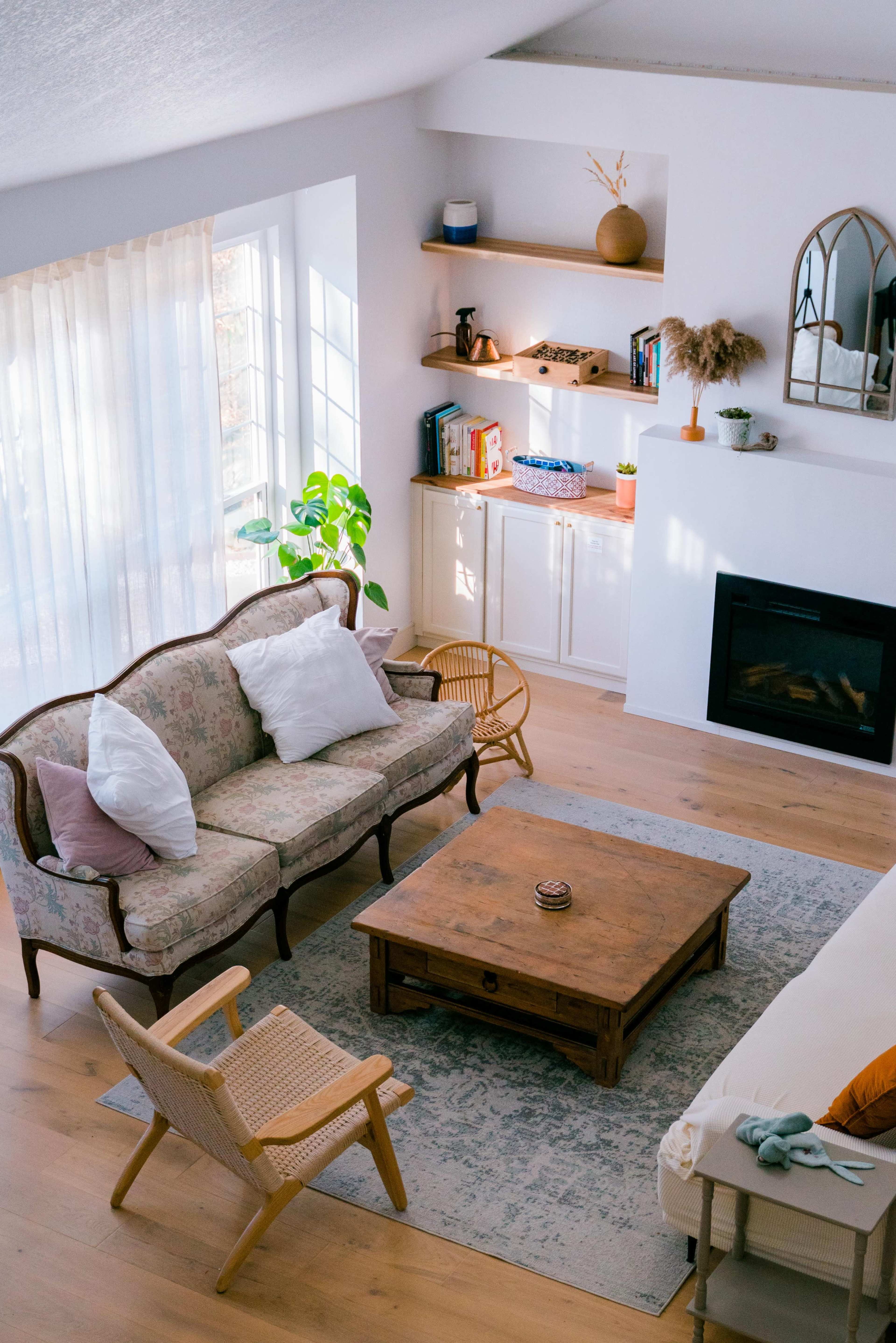 The image shows a cozy living room with a floral sofa, a wooden coffee table, a small armchair, and shelves displaying decorative items.