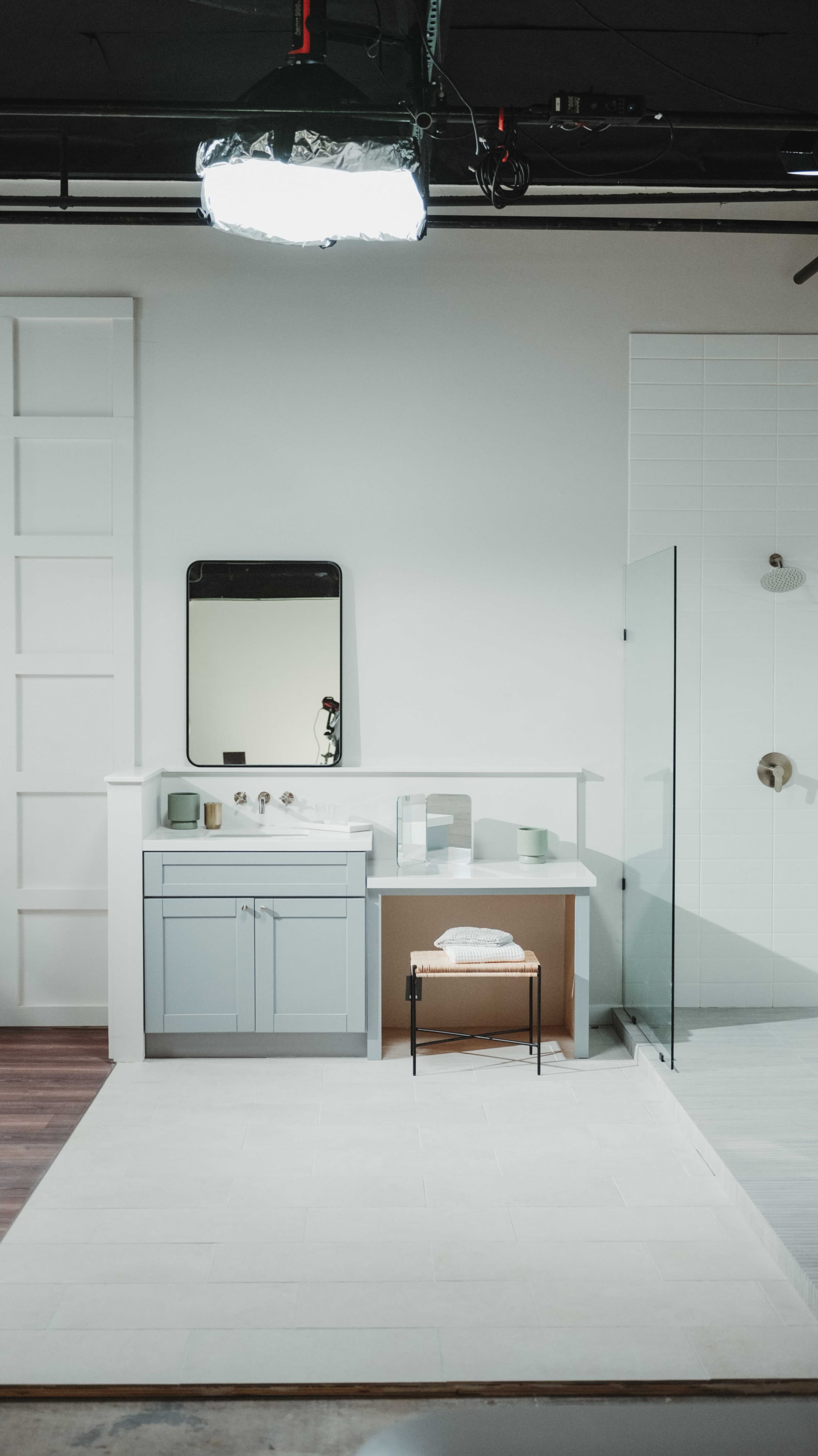 A modern bathroom featuring a light blue vanity with a mirror, a small bench, and a glass shower enclosure.