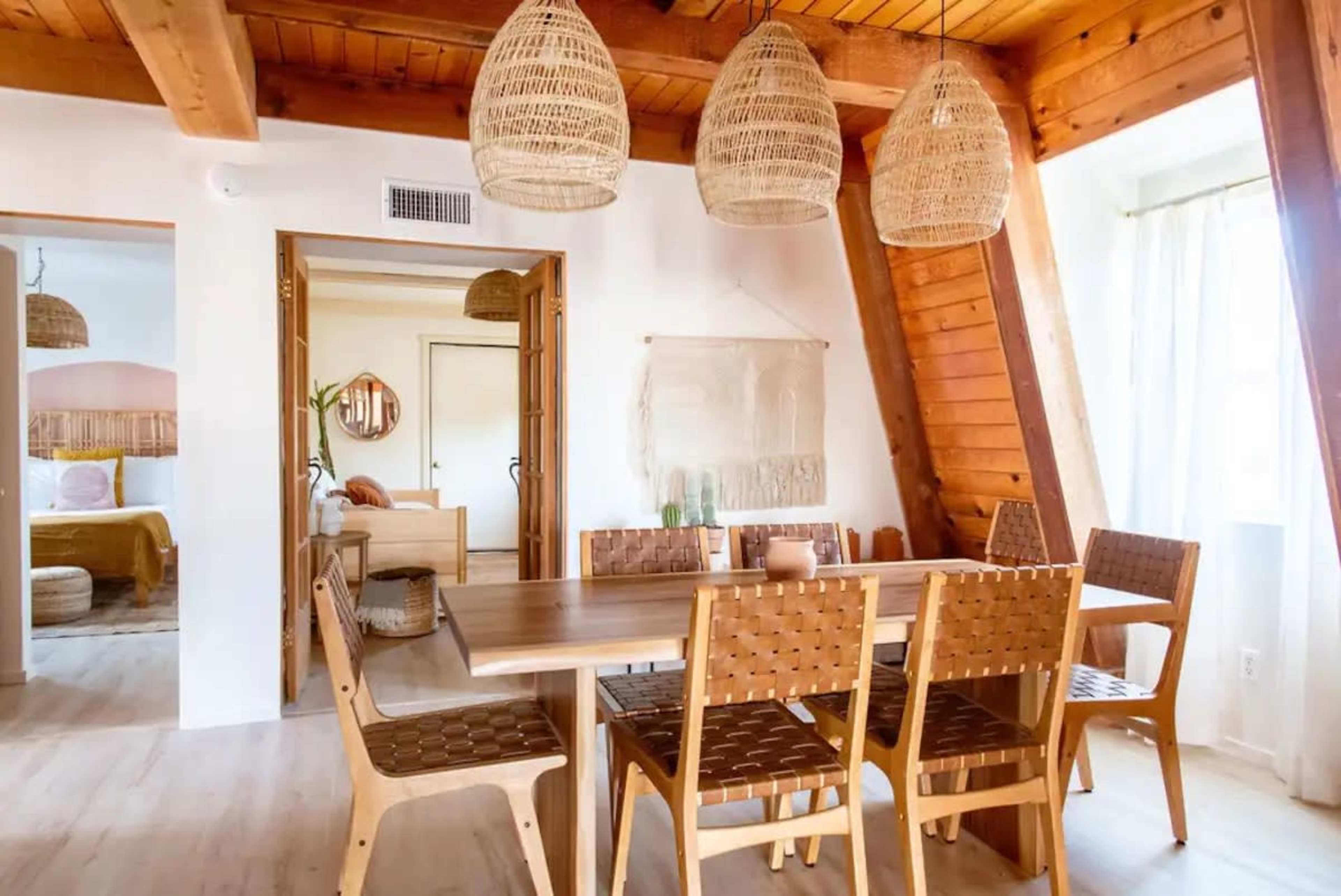 A wooden dining area with a large table surrounded by woven chairs, featuring three hanging light fixtures above.