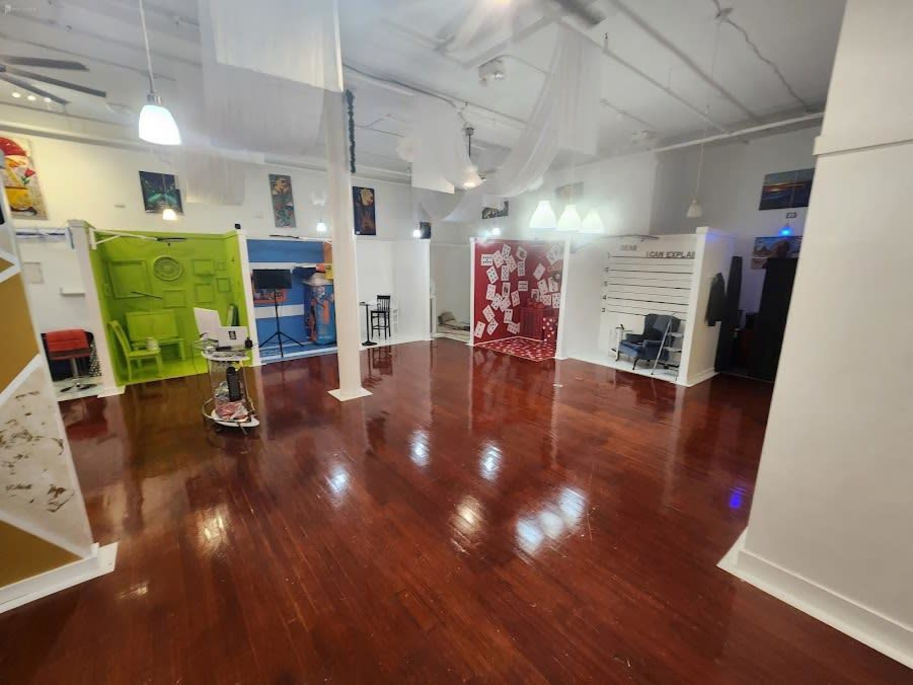 An empty, well-lit interior space with polished wooden floors, featuring colorful walls and different sections enclosed by partitions.