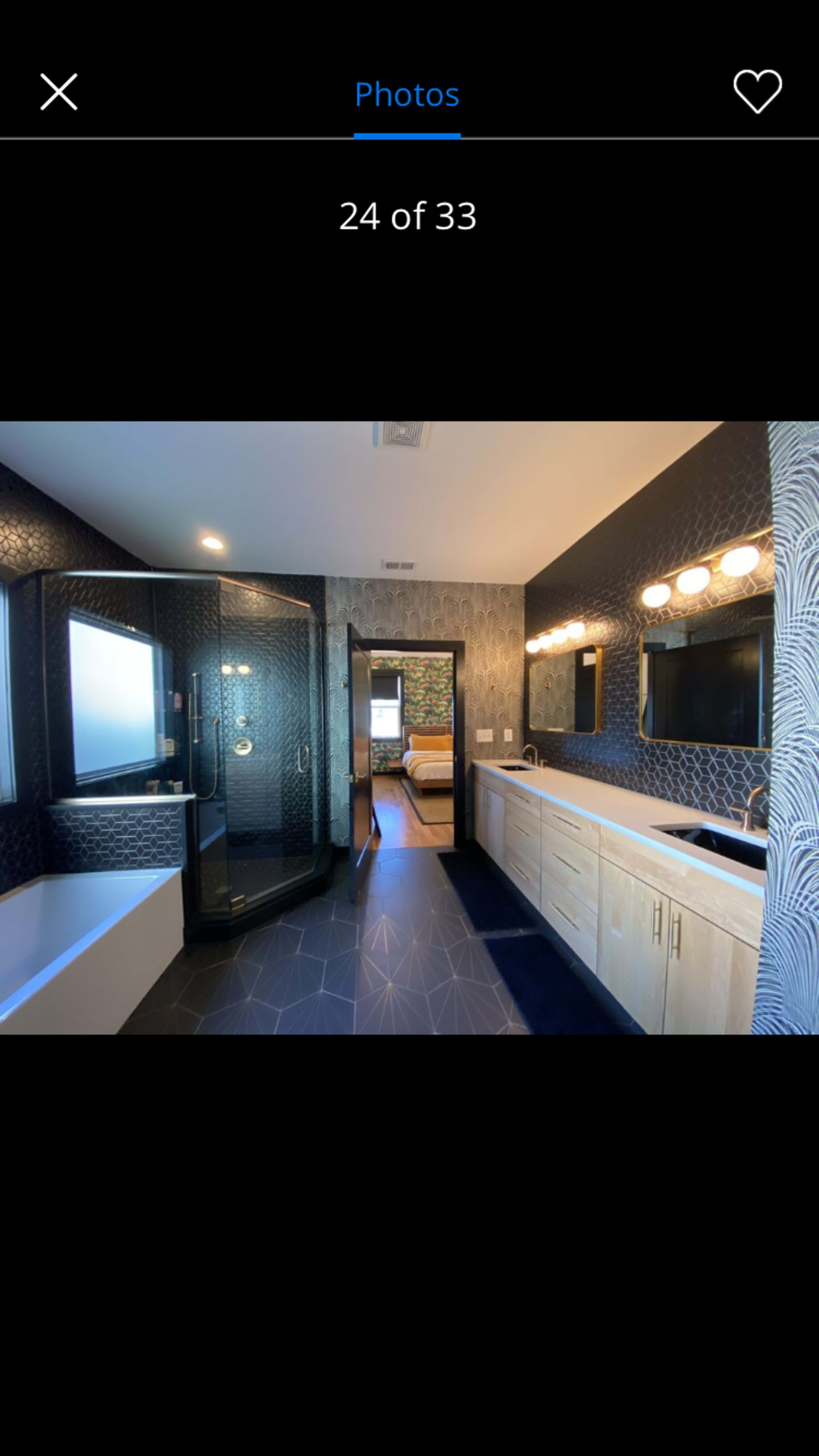 A modern bathroom featuring a walk-in shower, a freestanding bathtub, dual sinks with wooden cabinetry, and patterned wallpaper.