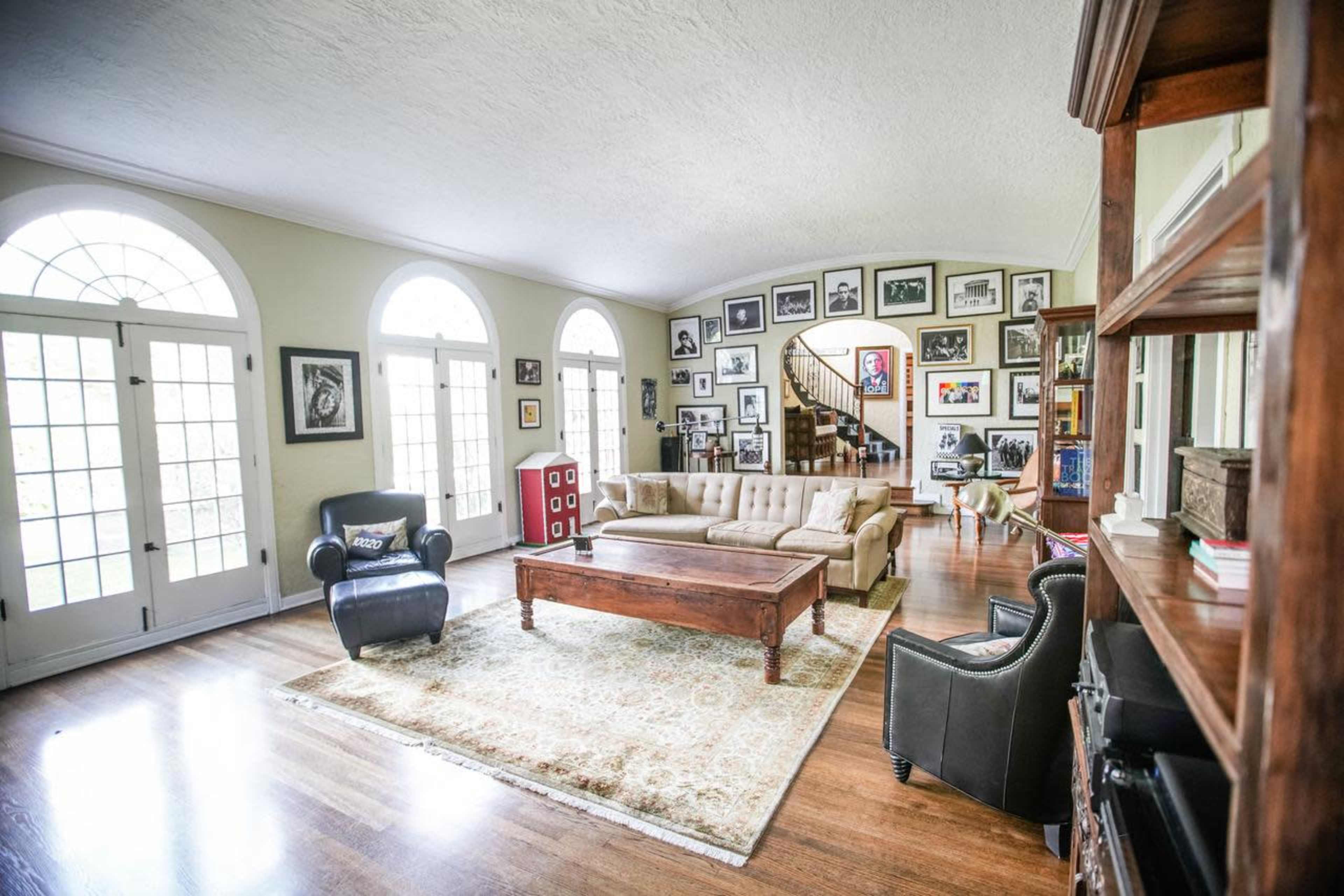 The living room features a sectional sofa, coffee table, and a large collection of framed photographs on the walls, with arched windows allowing natural light to enter.