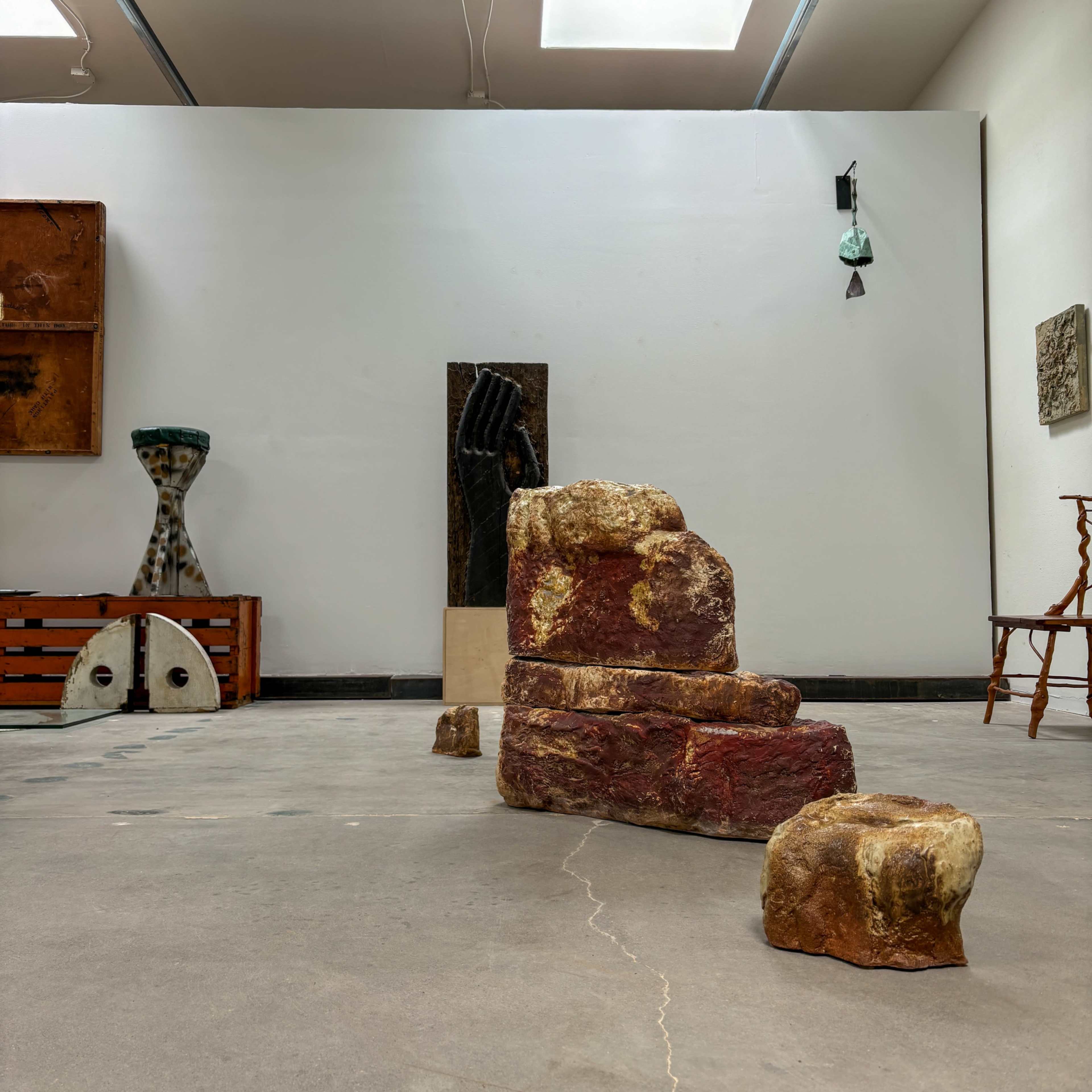 The image shows an art gallery featuring various sculptures and installations, including a series of staggered stone-like formations in the foreground.