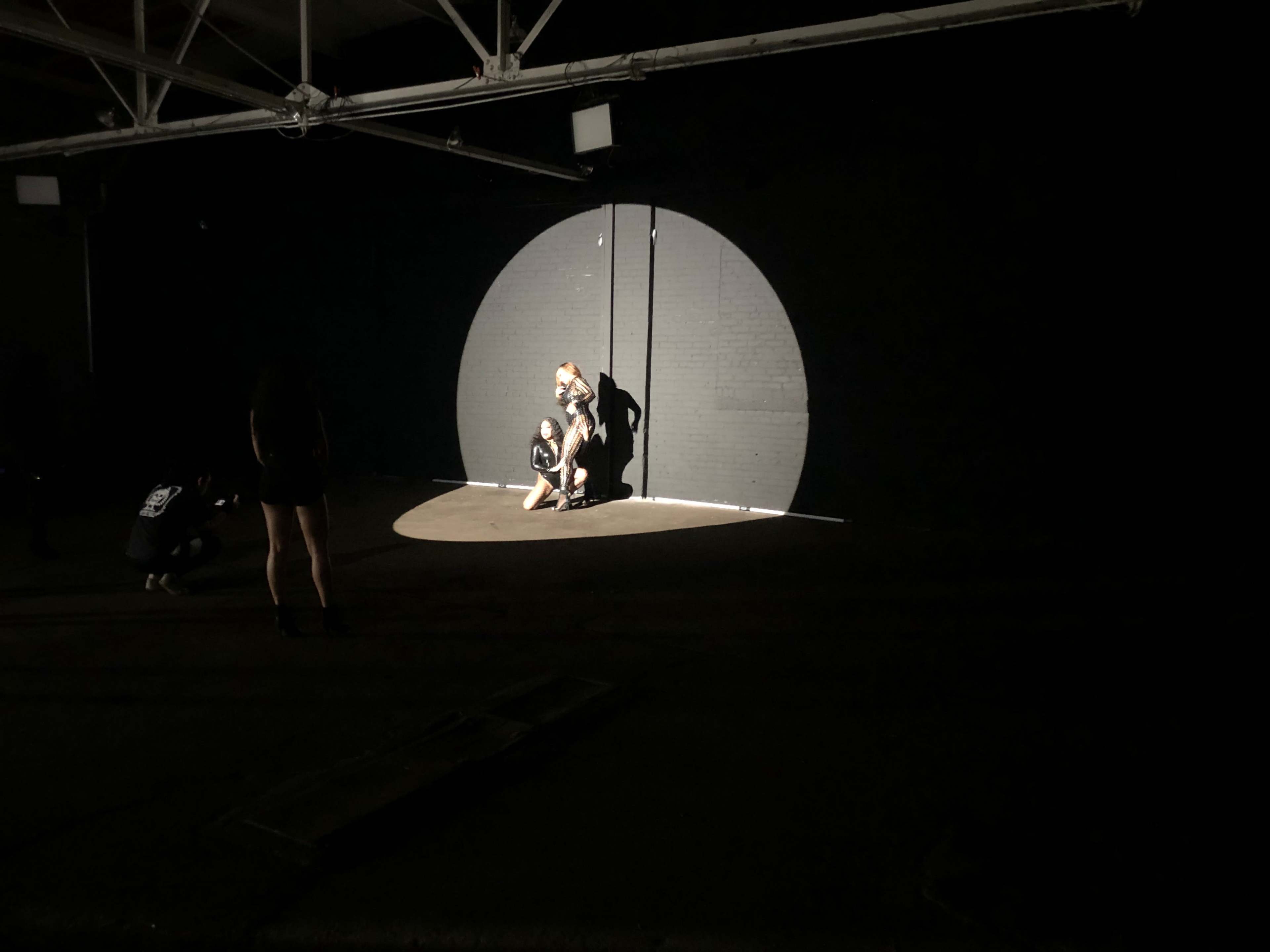 Two individuals in a spotlight on a dark stage, while another person stands in the background.