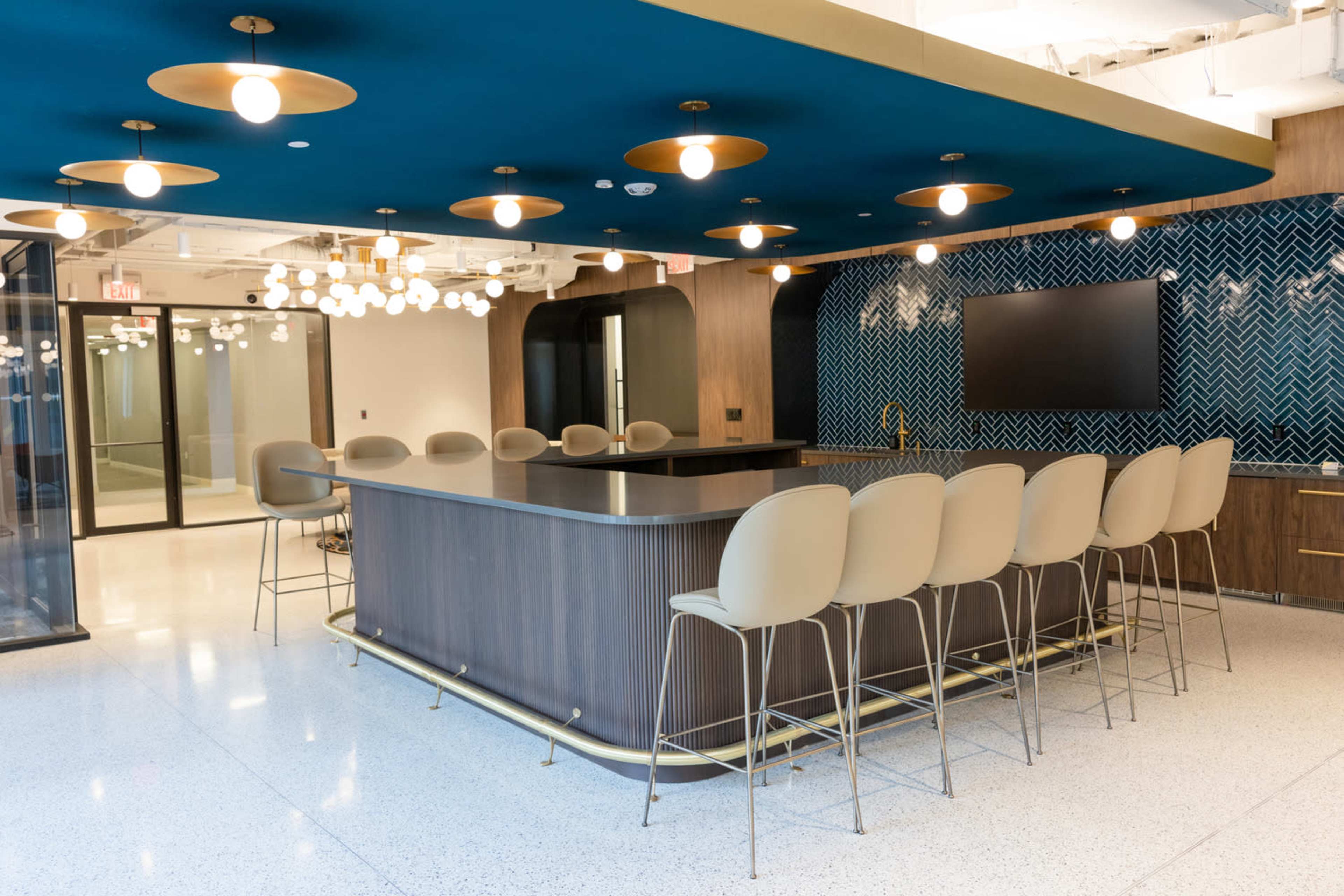 A modern kitchen area features a large central island with bar seating and pendant lights, set against a blue ceiling and patterned wall.
