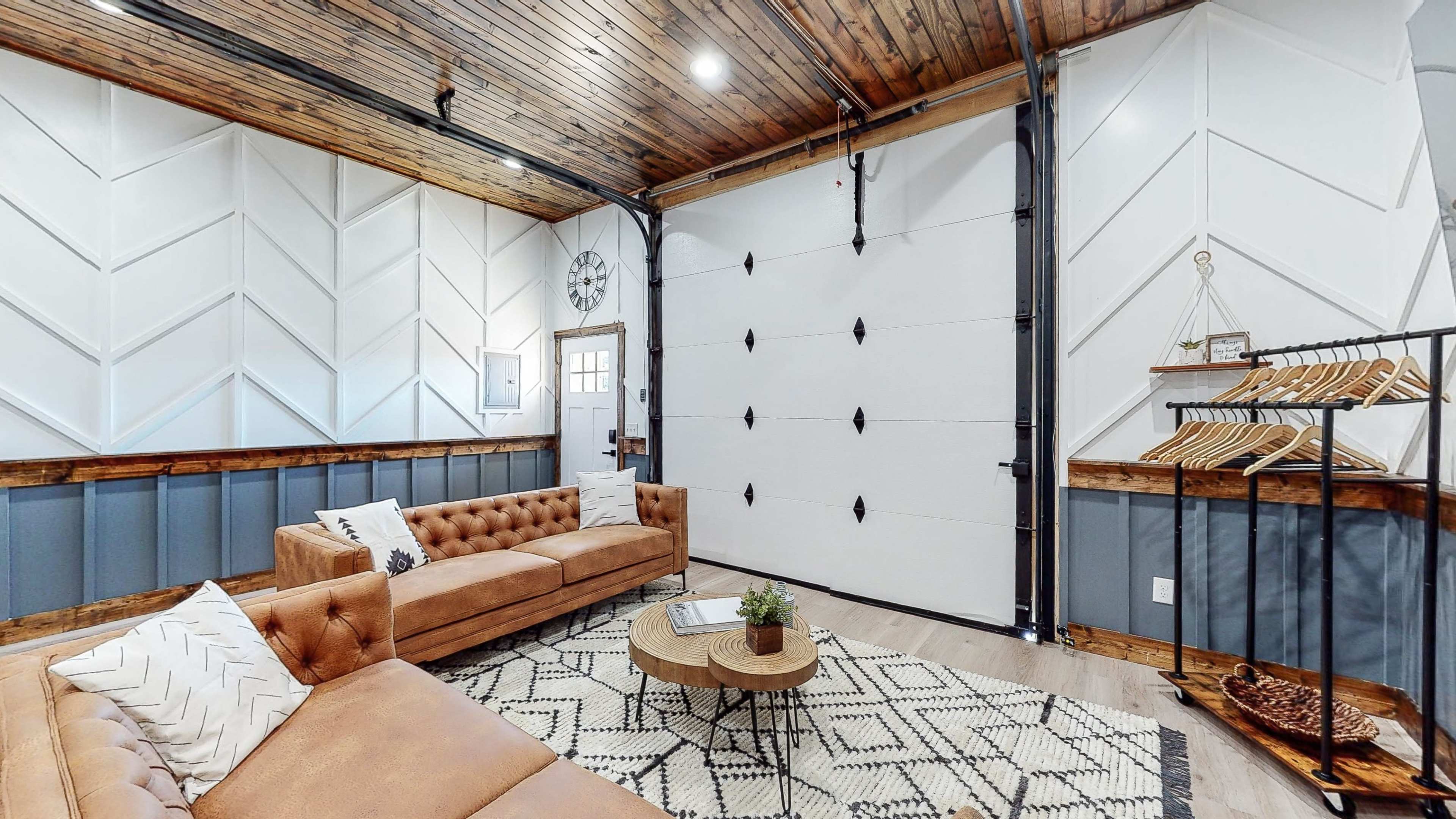 The room features a cozy seating area with a brown tufted sofa, a round coffee table, and a wall-mounted coat rack, all set against a backdrop of wooden ceiling and patterned walls.