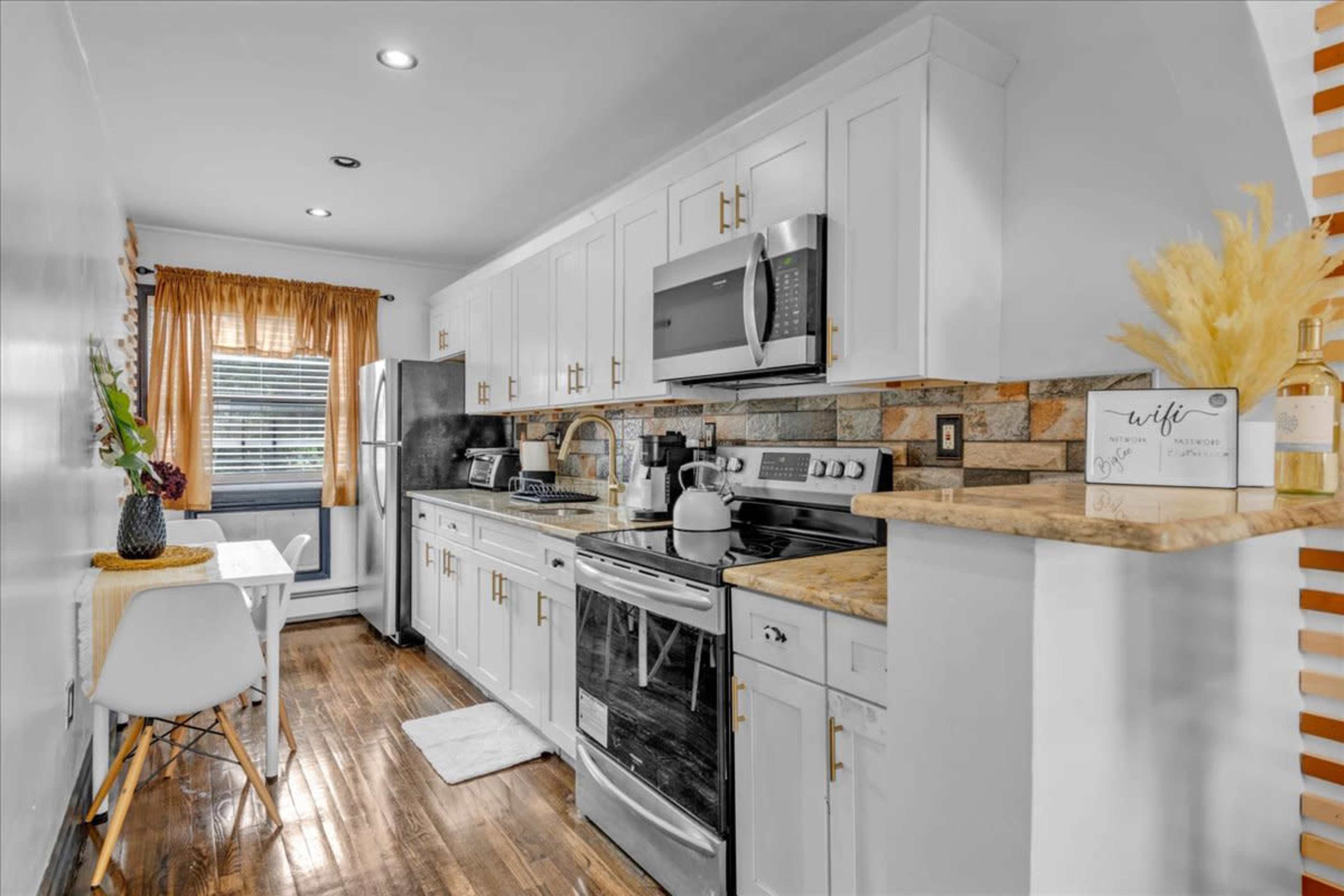 A modern kitchen with white cabinetry, a stainless steel refrigerator, and a small dining table by the window.