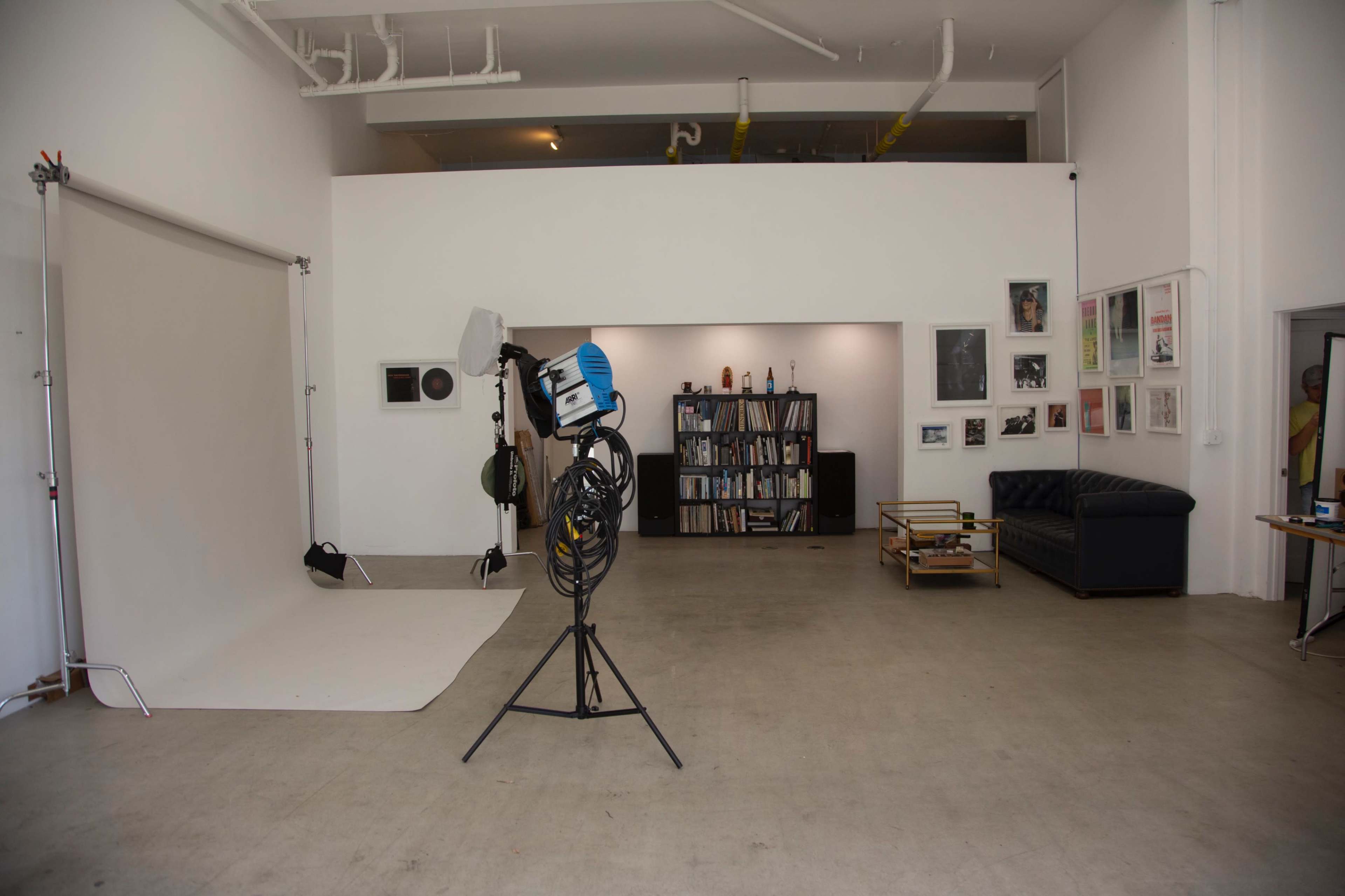 A photography studio with a backdrop setup, lighting equipment, a bookshelf, and a couch in a spacious room.