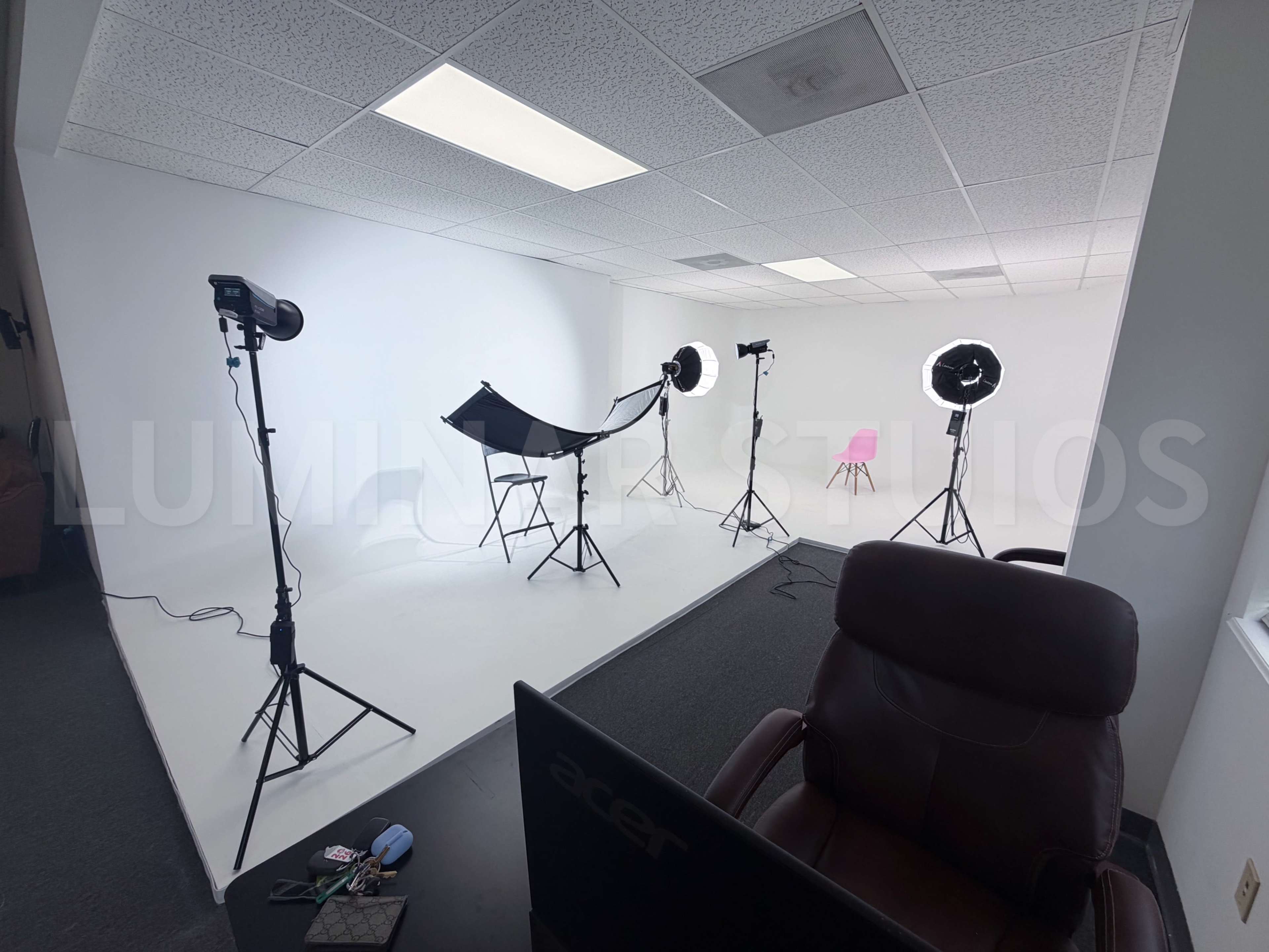The image shows a photography studio equipped with various lighting setups and a minimalist backdrop.