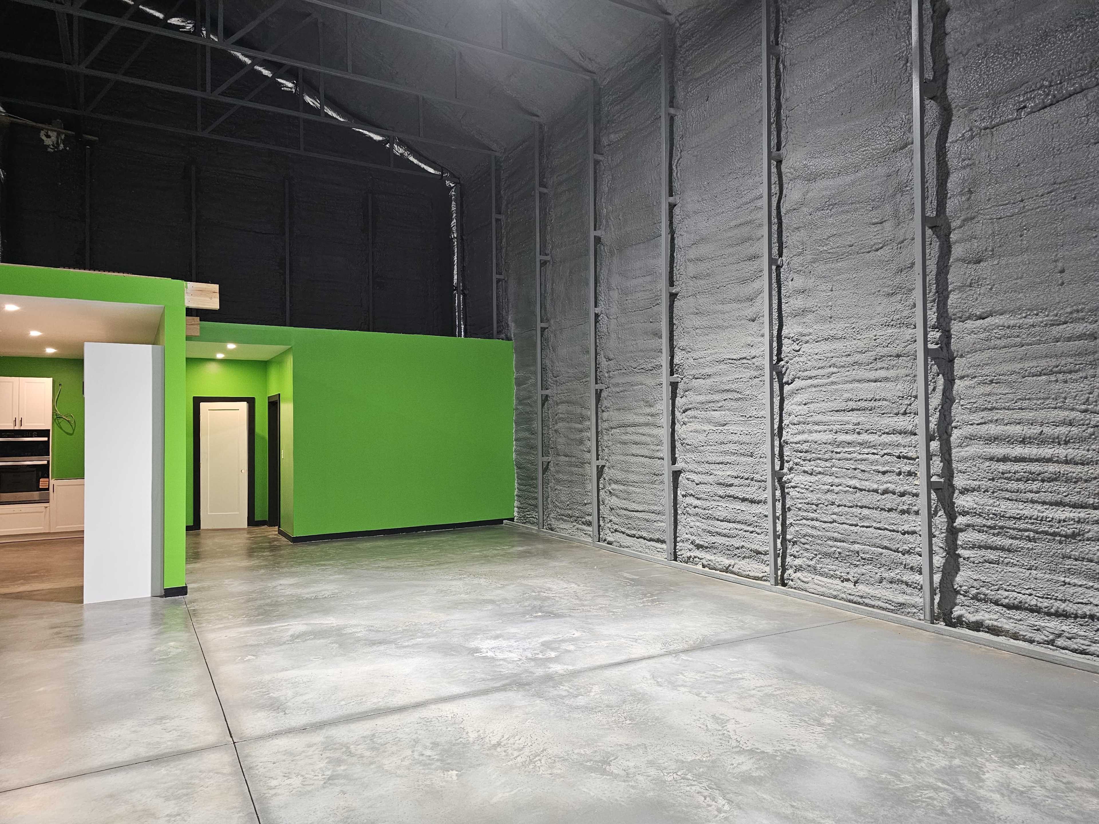 The image shows a spacious, partially finished interior of a building with a green accent wall and a polished concrete floor.