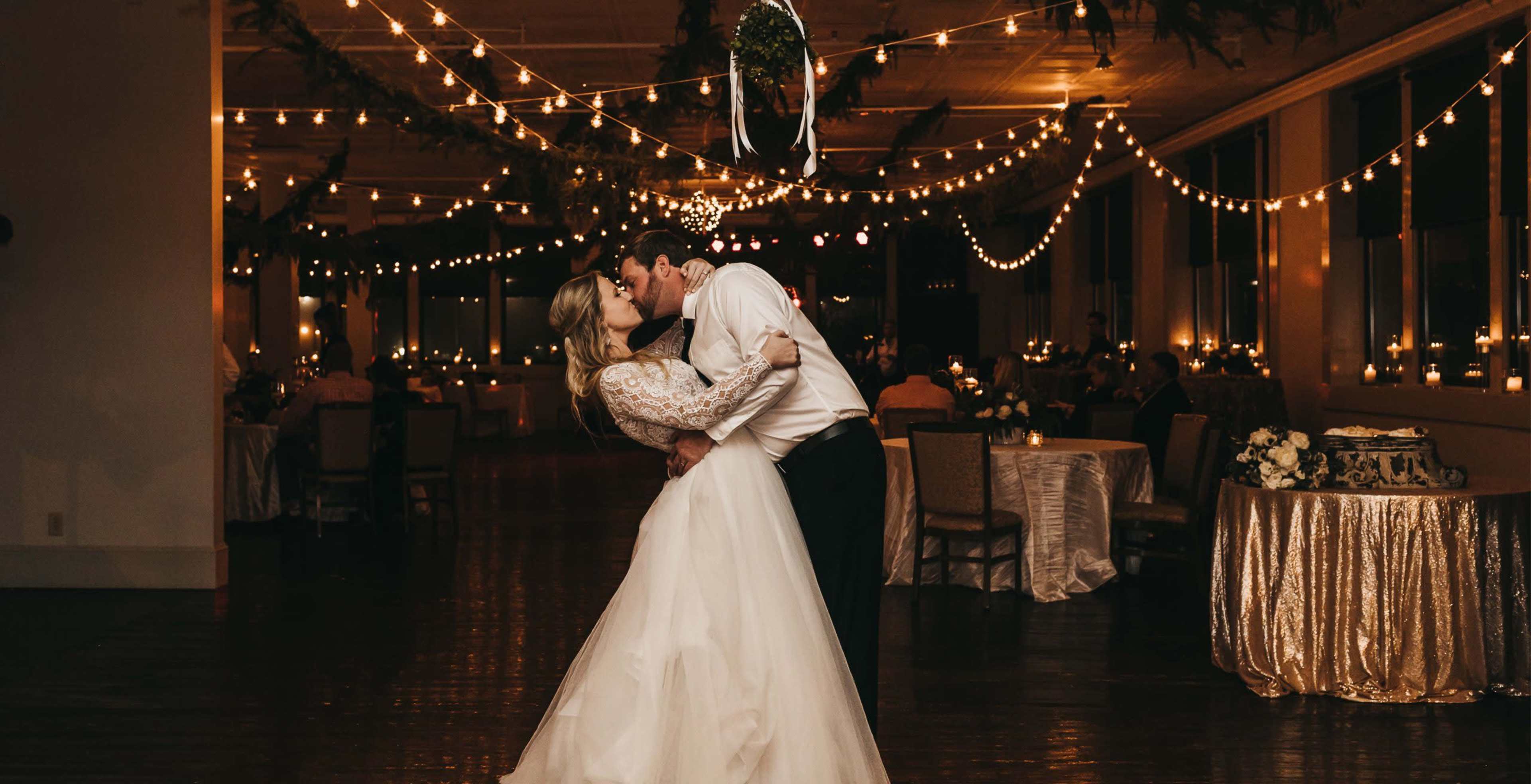 A newlywed couple dances closely under soft, twinkling lights in an elegantly decorated reception venue.