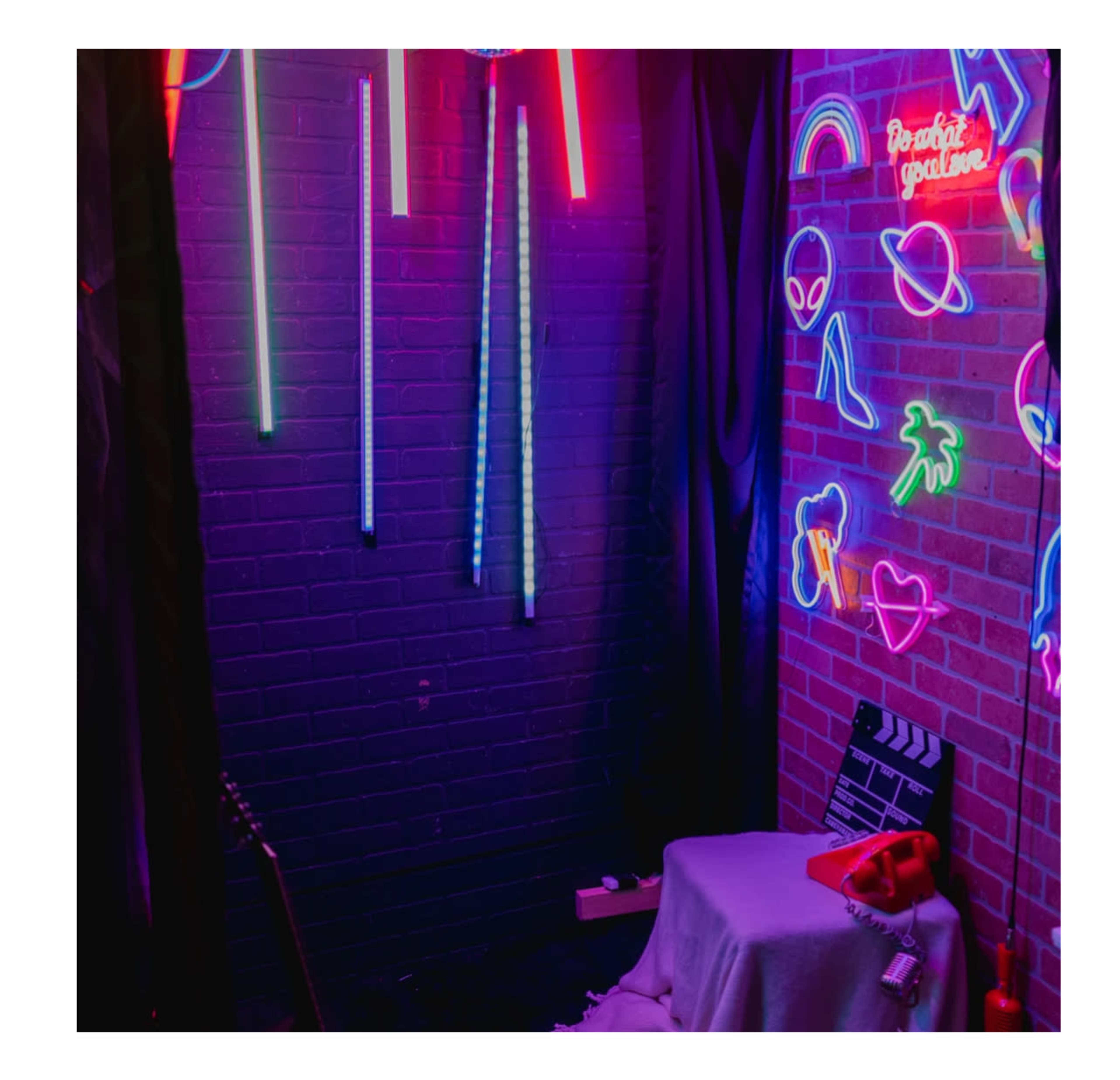 A dimly lit room with colorful neon lights and signs on the walls, featuring a small table covered with a cloth and a red telephone in the foreground.