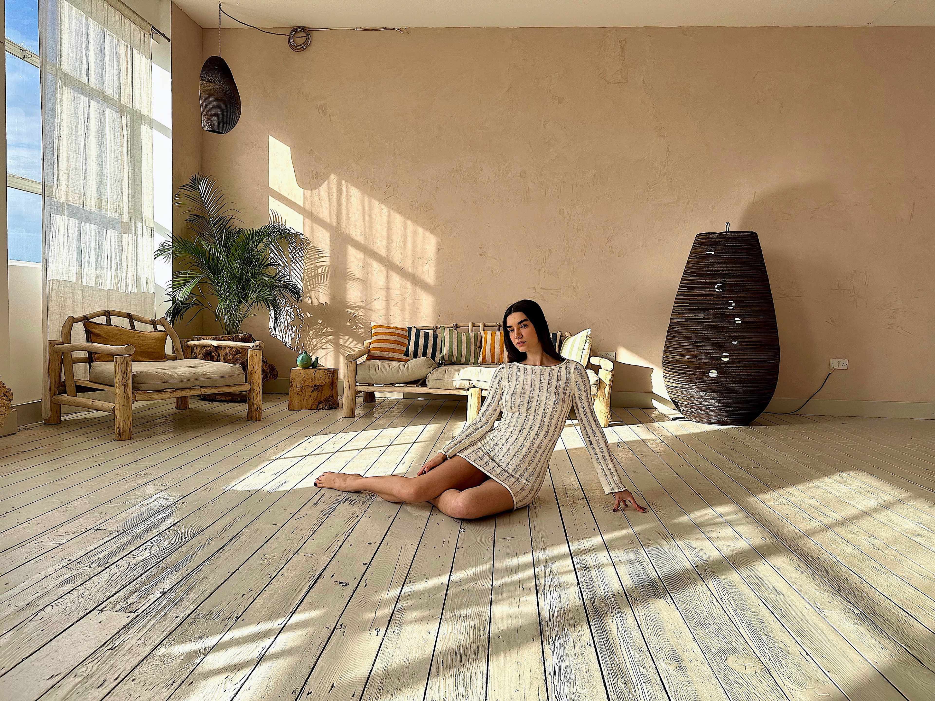 A person sits on the floor of a spacious, lightly decorated room with natural light streaming through large windows.