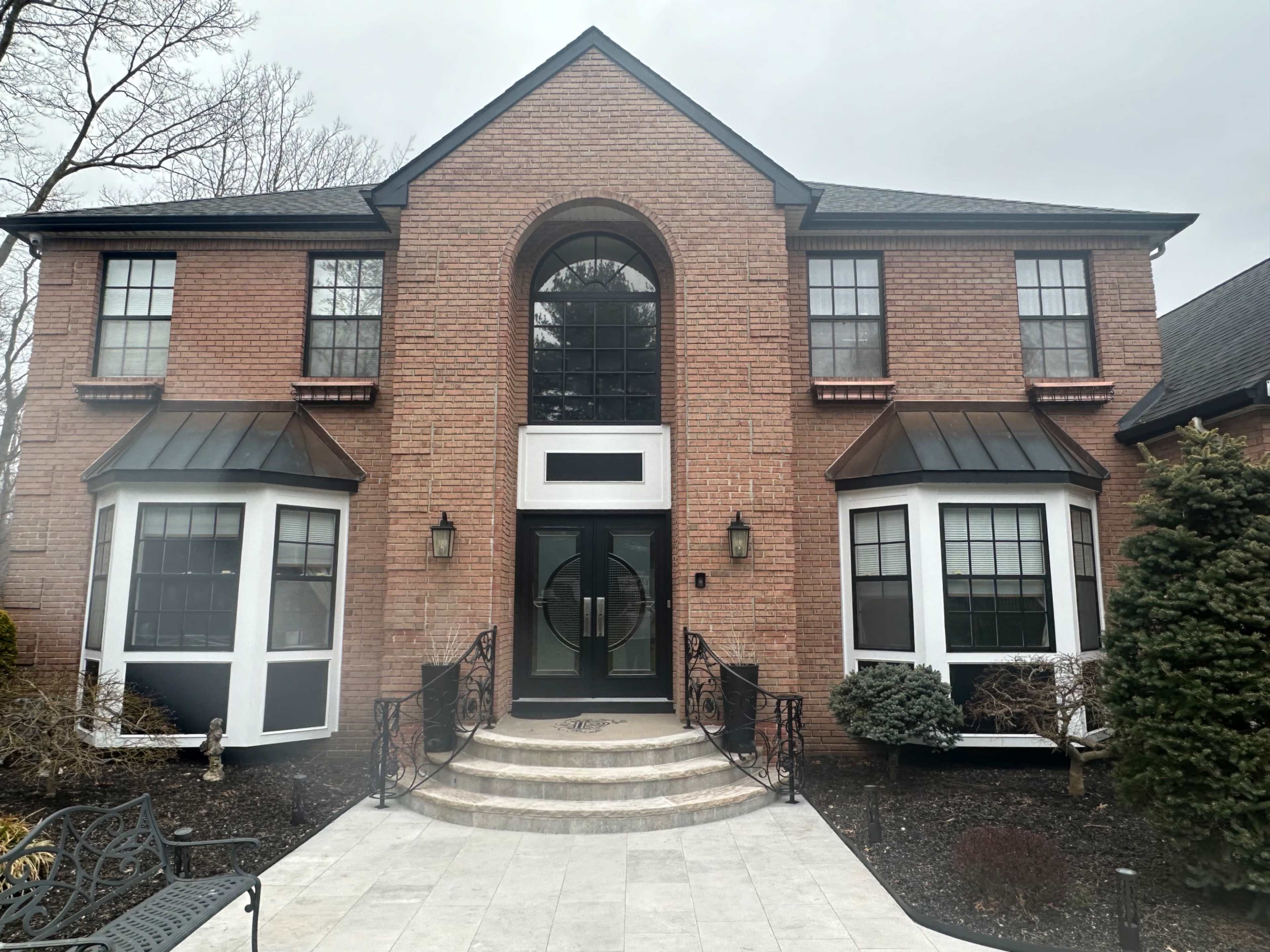 A two-story brick house with a central arched entrance, flanked by large windows on either side, and a stone walkway leading to the front door.