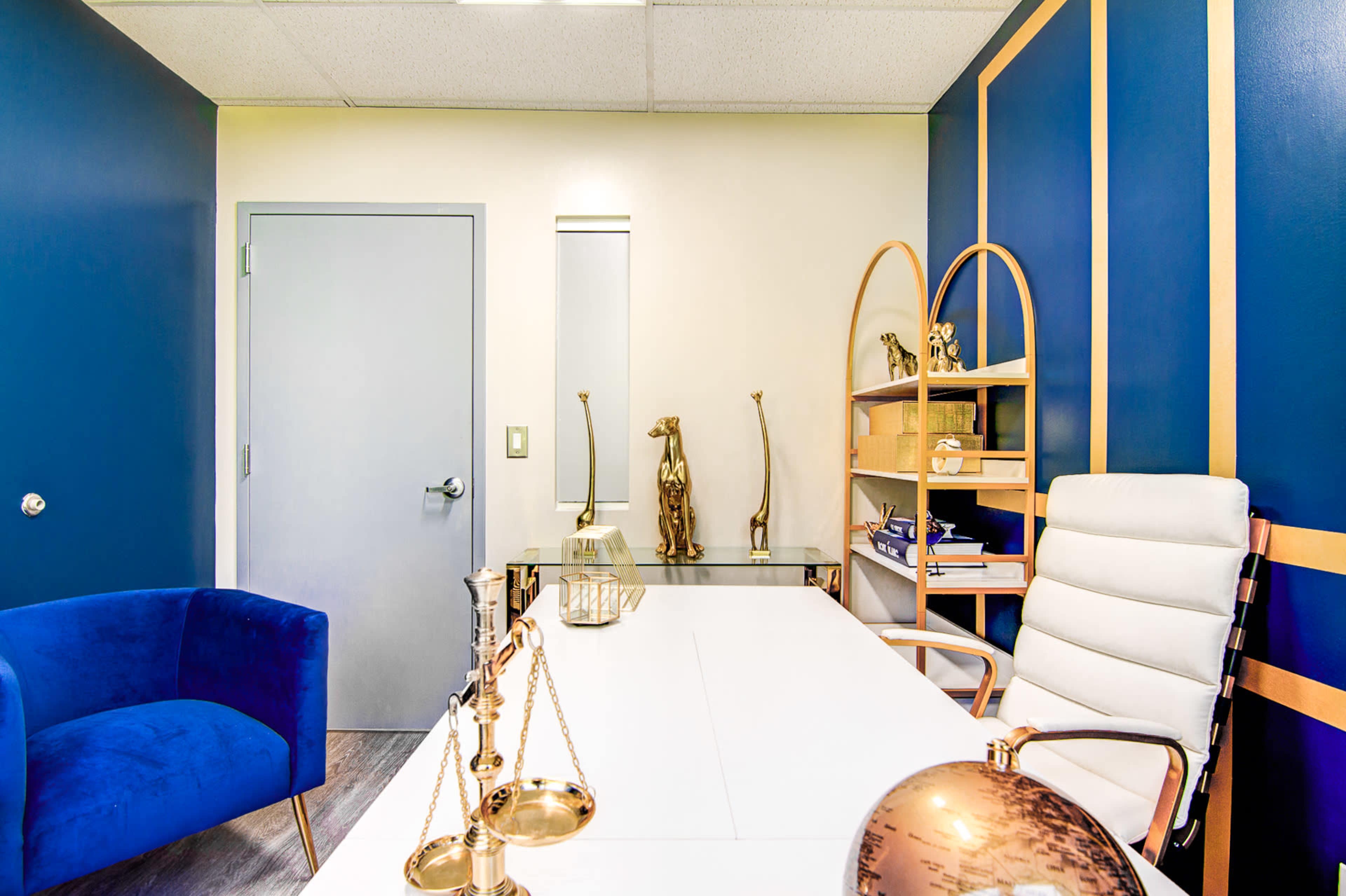 A modern office space featuring a white desk, a leather chair, blue walls, and various decorative items, including sculptures and a globe.