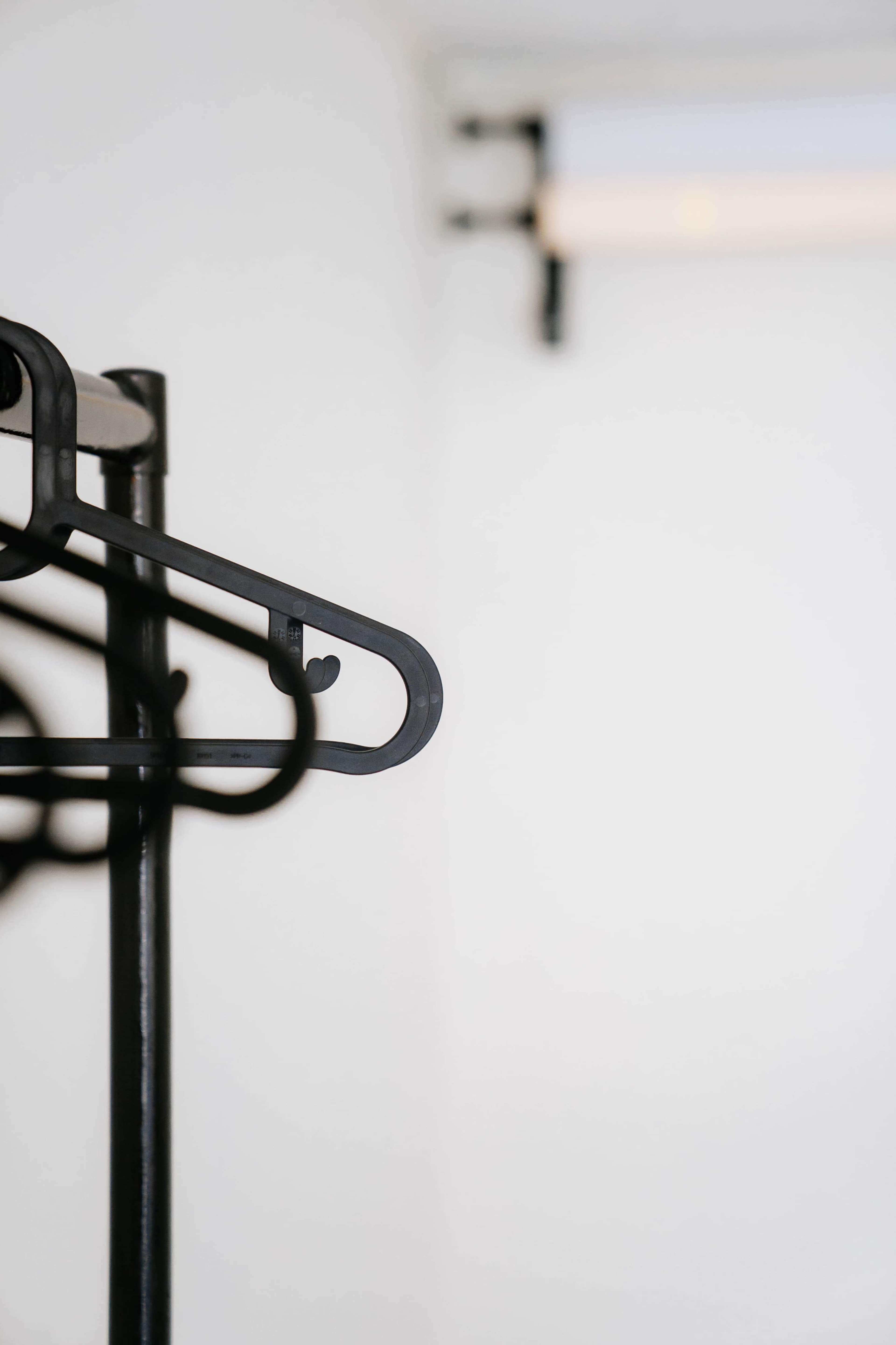 A black metal coat hanger is mounted on a simple wall in a lightly lit space.