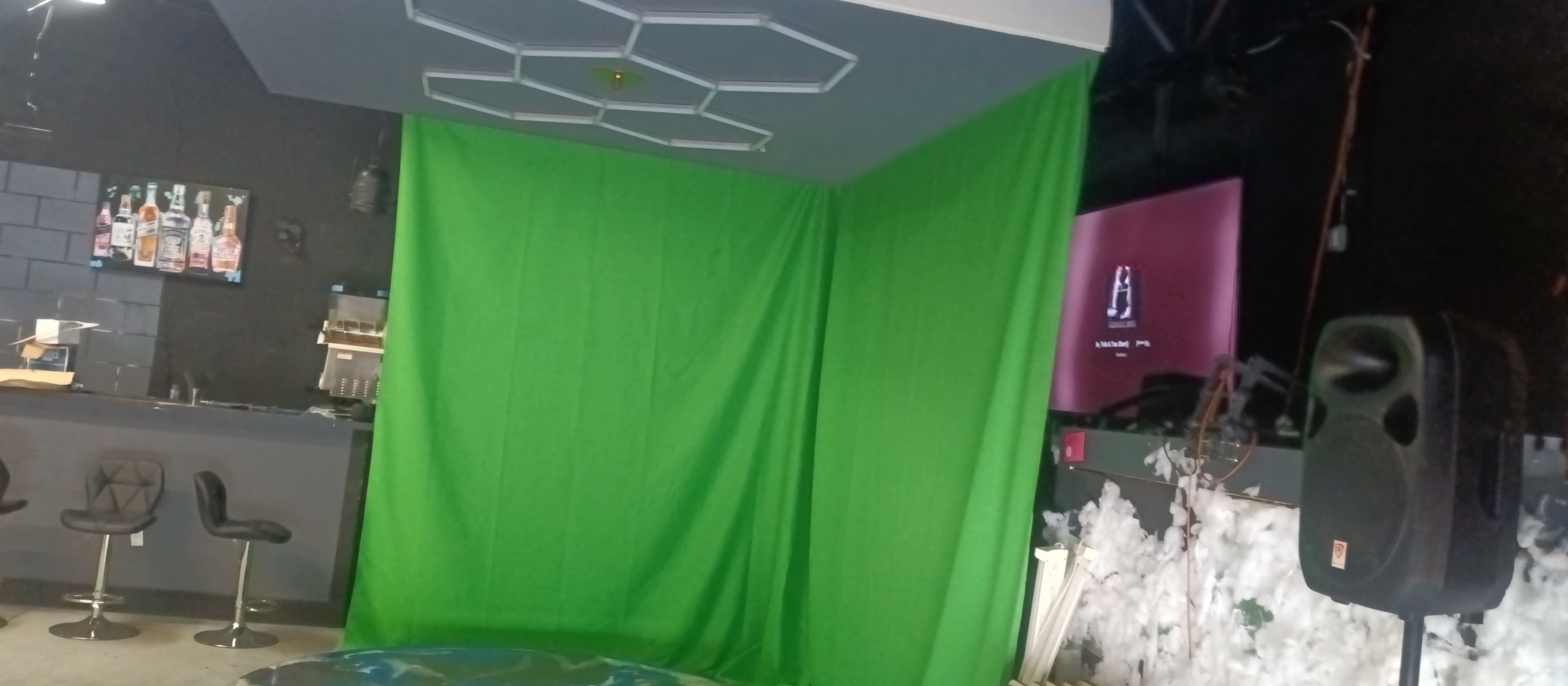 A green screen setup in a dimly lit space, with a bar in the background and a TV displaying a static screen.