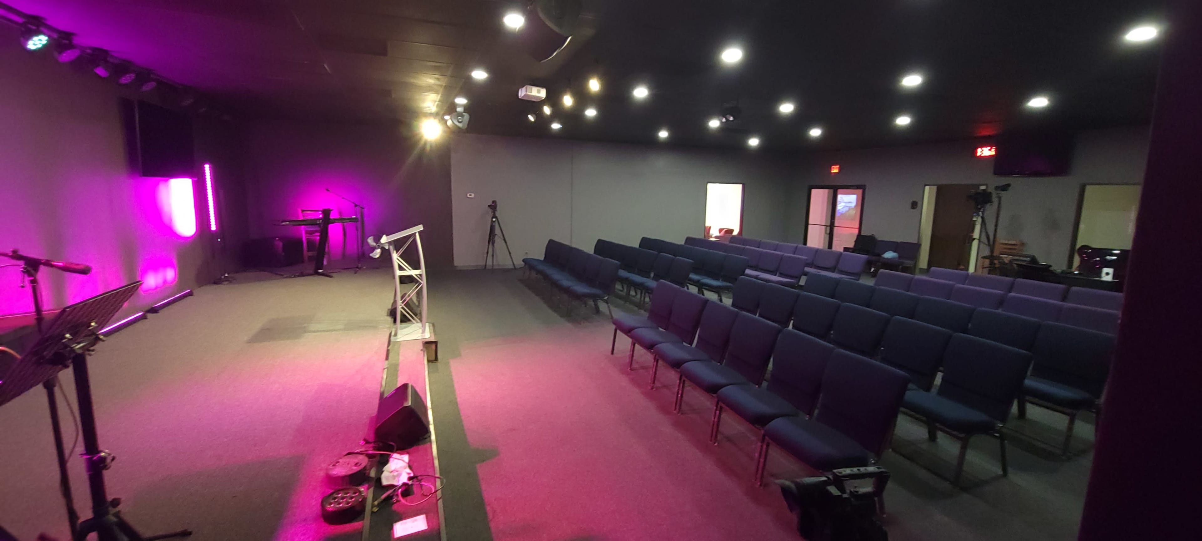 The image shows an empty church auditorium with rows of blue chairs, a stage with a podium, and soft lighting.
