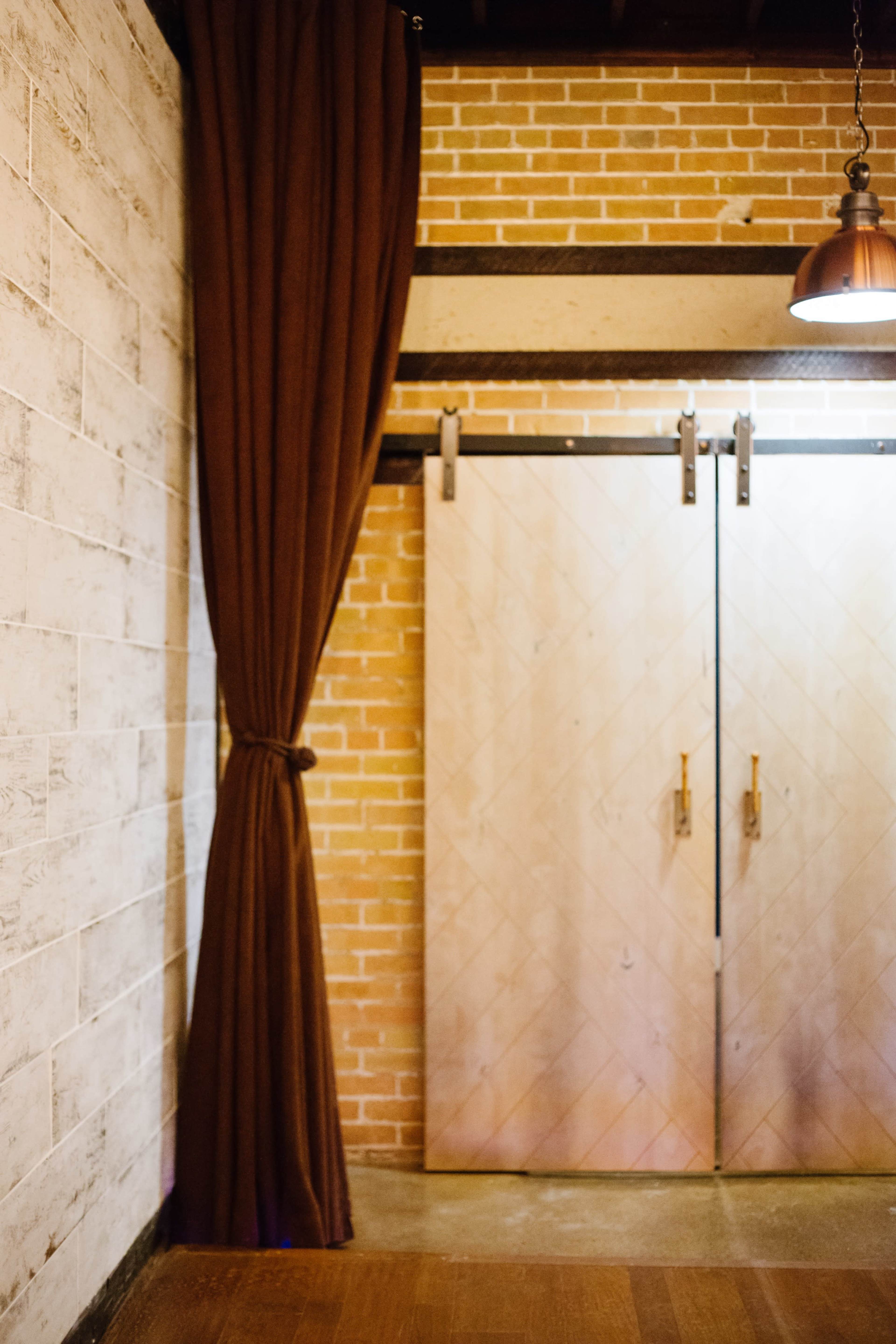 A wooden sliding door with metal handles next to a brown curtain in a room with brick and wooden walls.
