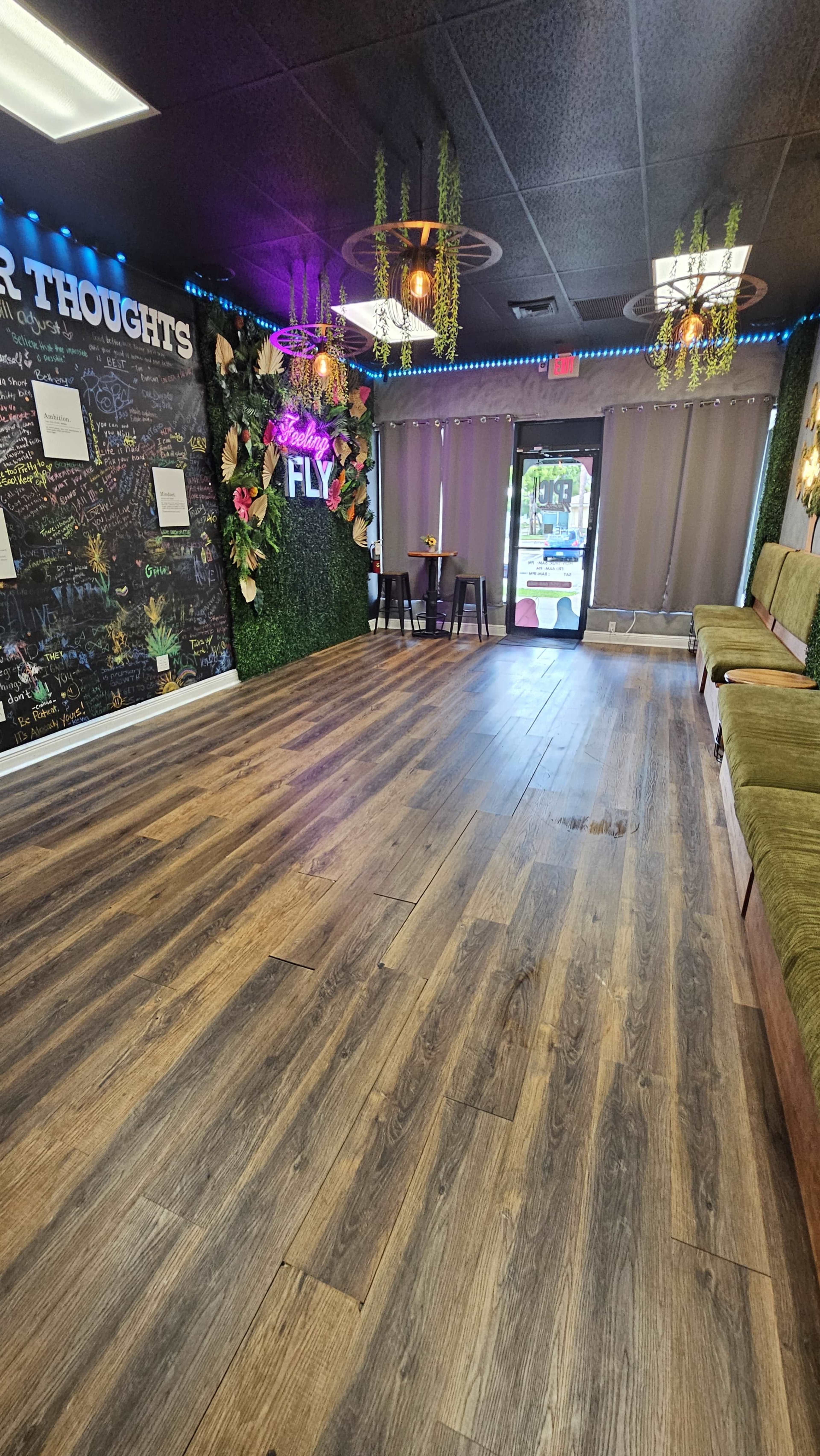 The image shows an indoor space with dark wood flooring, green seating along one wall, a colorful mural on another, and a doorway leading outside.