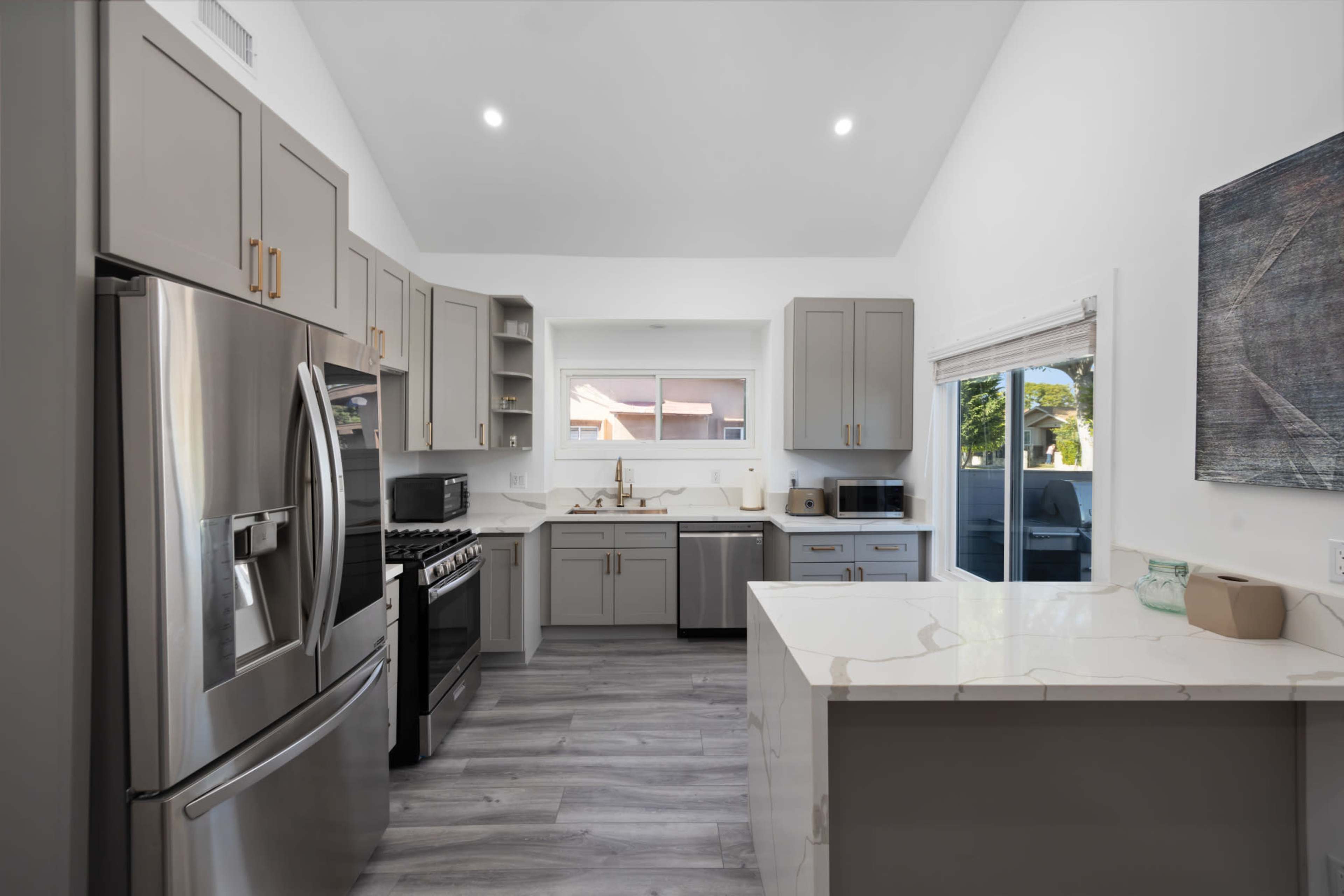 A modern kitchen featuring gray cabinetry, stainless steel appliances, and a large island with a white countertop.
