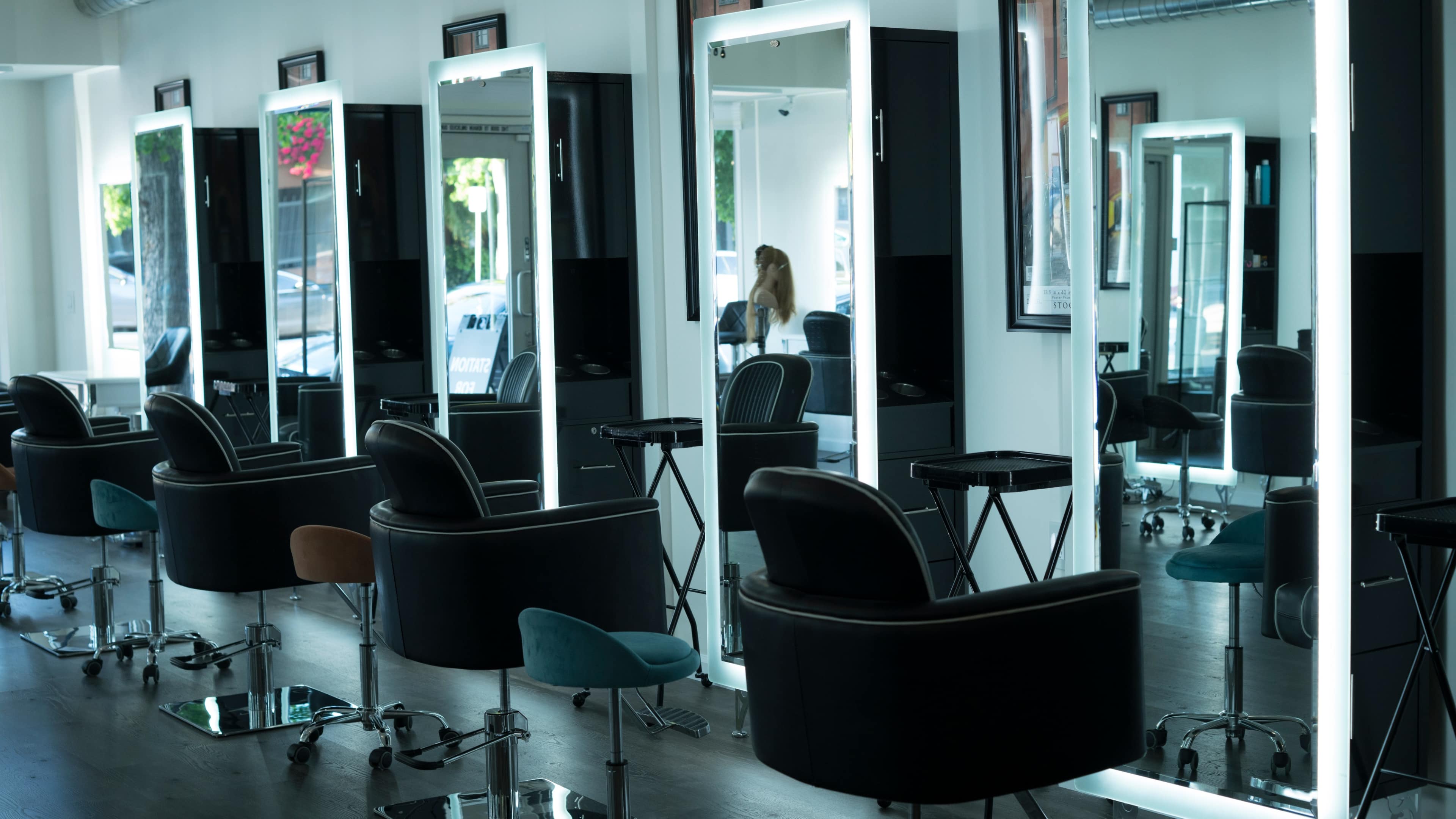 A modern hair salon with several black styling chairs facing illuminated mirrors.
