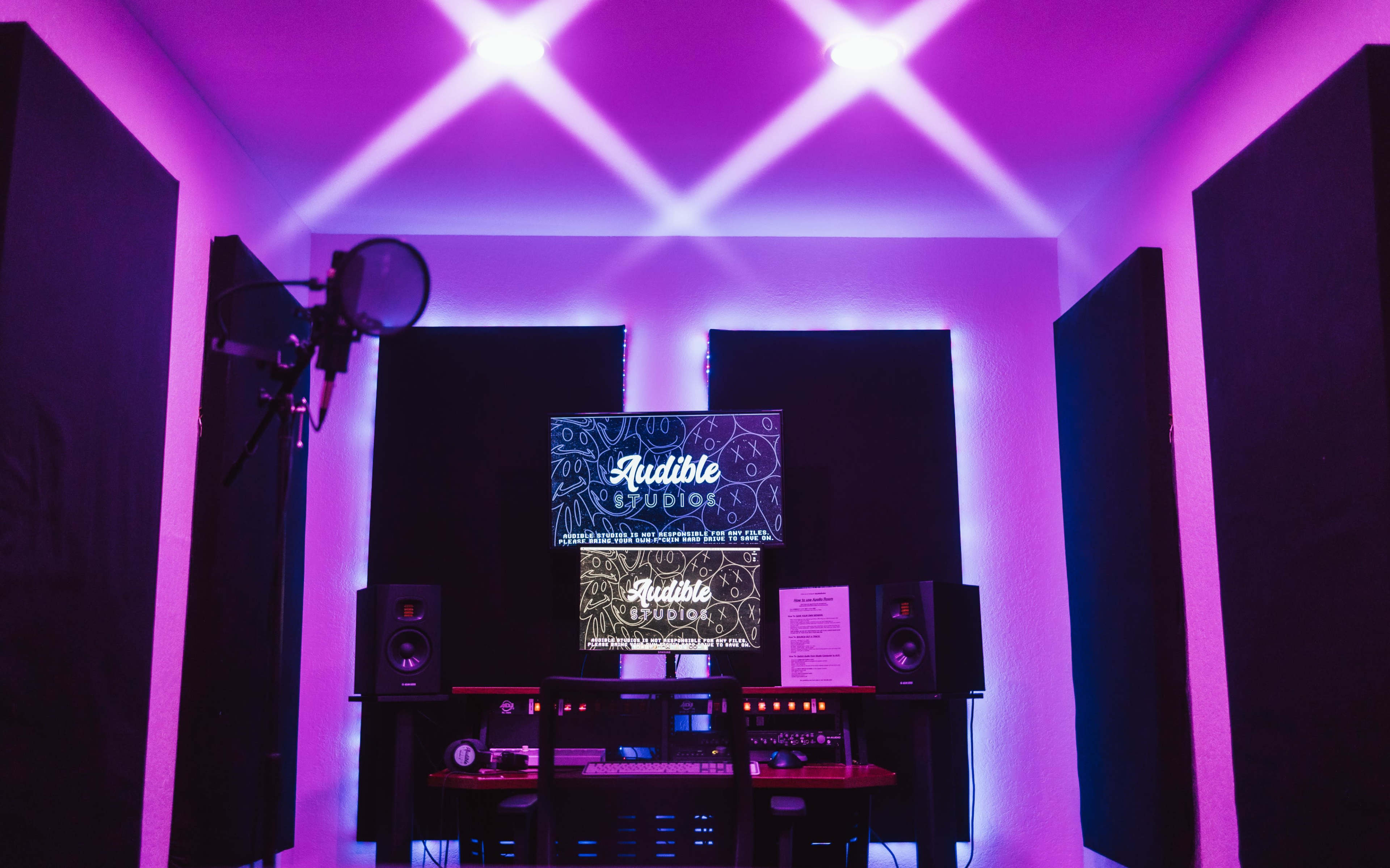 A recording studio with purple lighting, featuring soundproof panels, a microphone, and audio equipment.