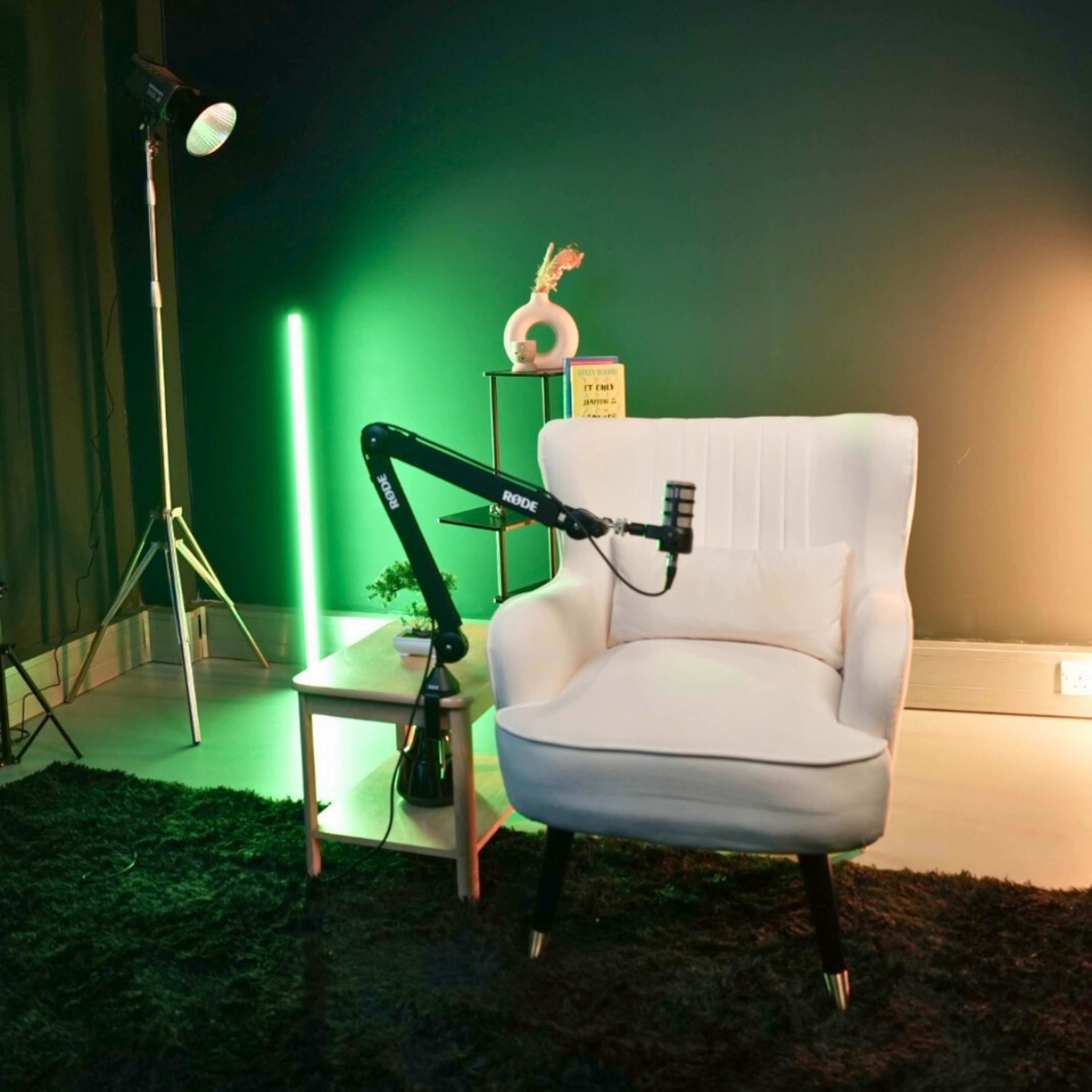 The image features a modern white armchair next to a small table, with a microphone mounted on an adjustable arm and illuminated by colorful lighting.