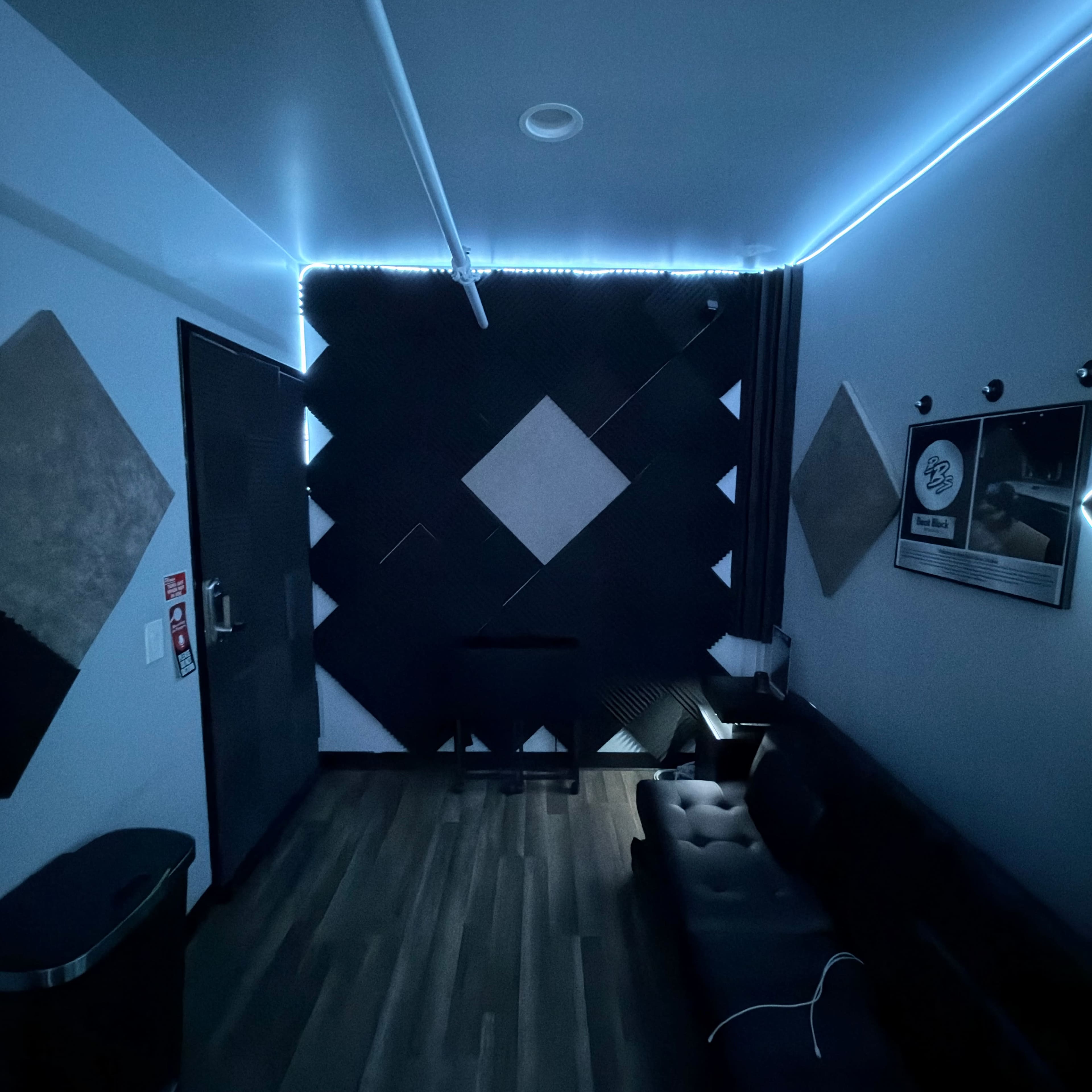 The image shows a modern recording studio with soundproofed walls, a couch, and ambient LED lighting.