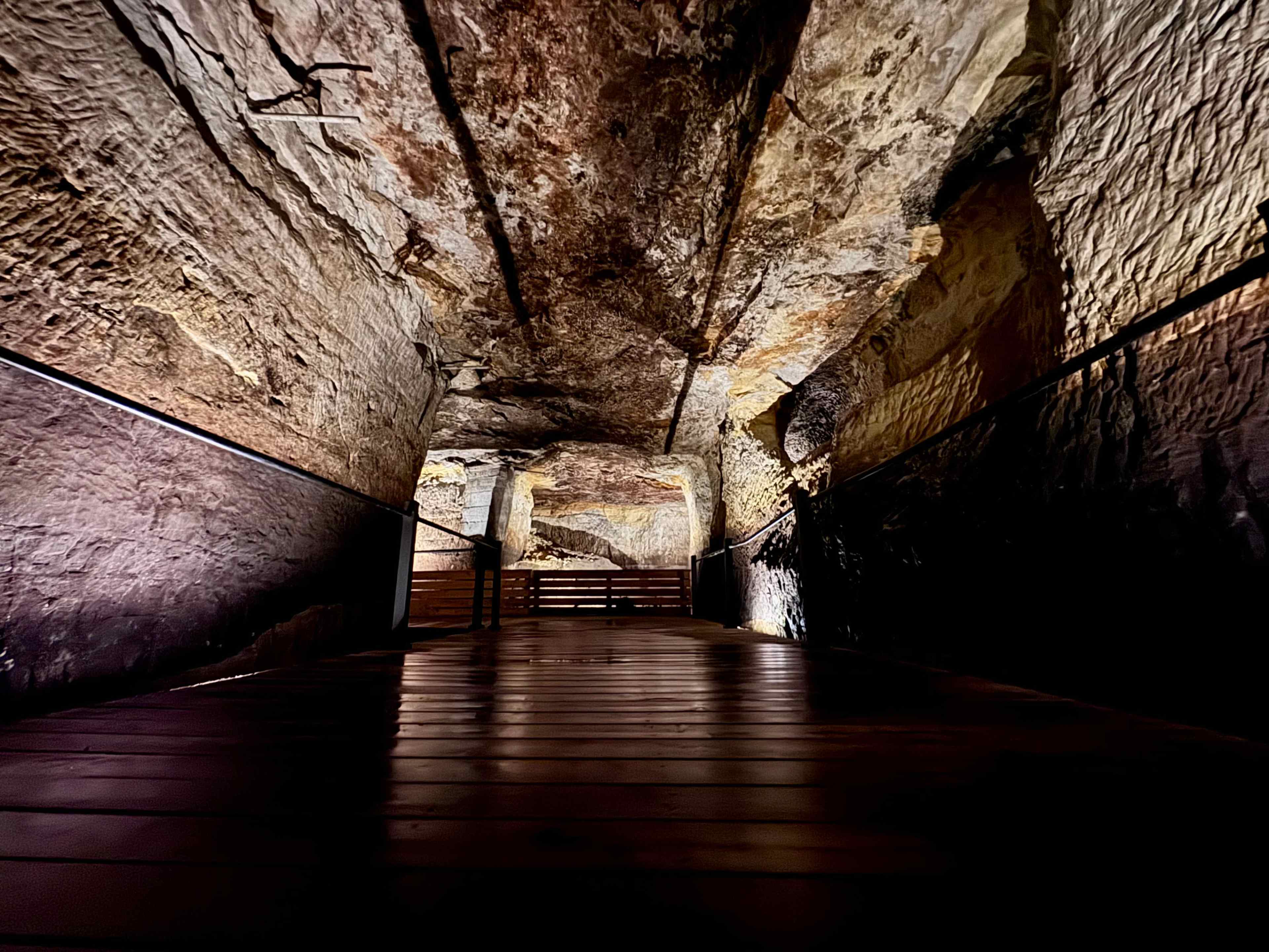 The image shows a dimly lit cavern with textured rock walls and a wooden floor.